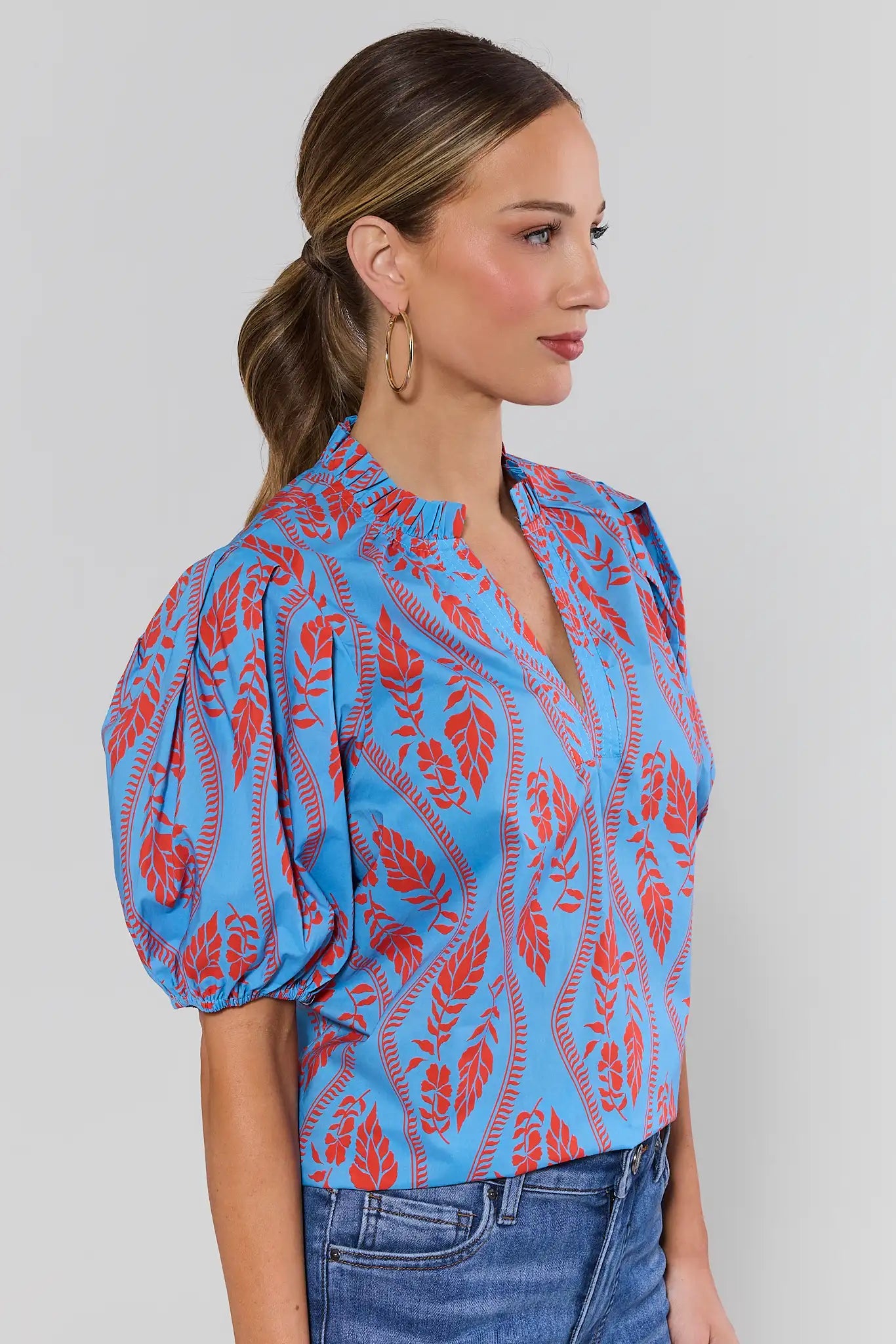 side shot Woman wearing a blue and red patterned blouse with puffed sleeves on a plain background