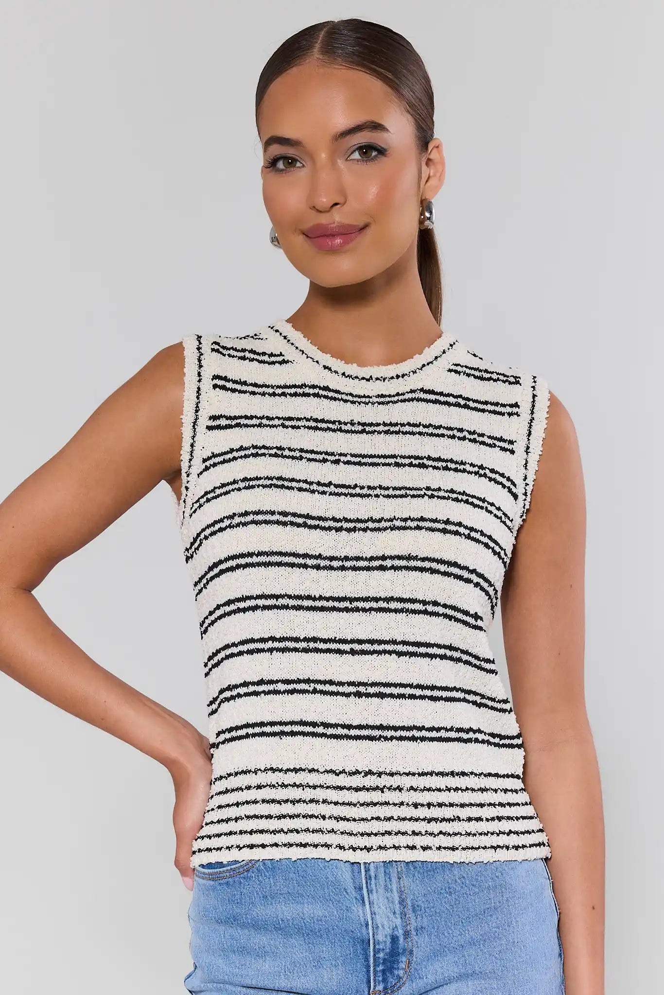 Woman wearing a sleeveless striped top and jeans on a plain background