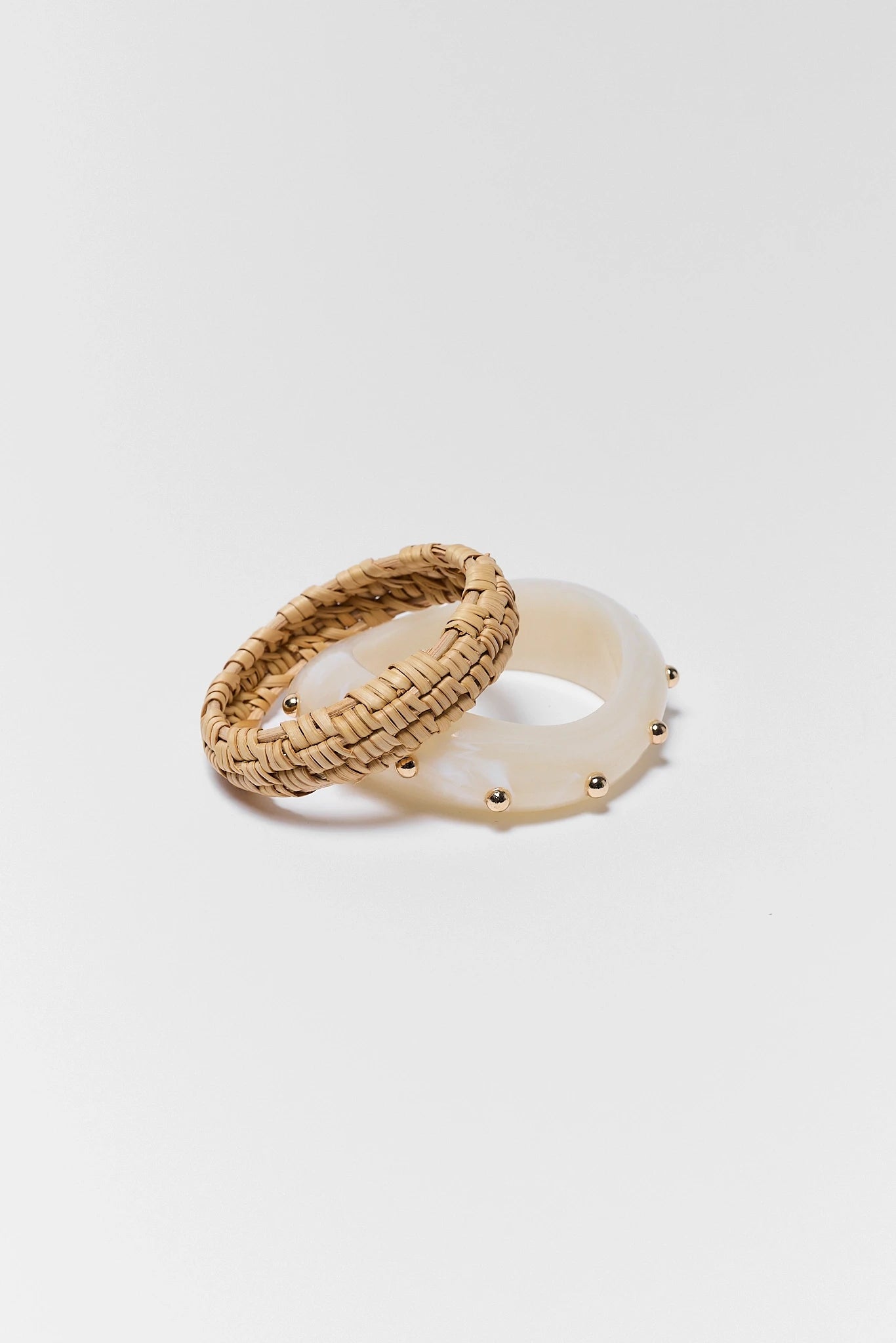 Two bangles, one woven and one with a shell-like finish, on a white background