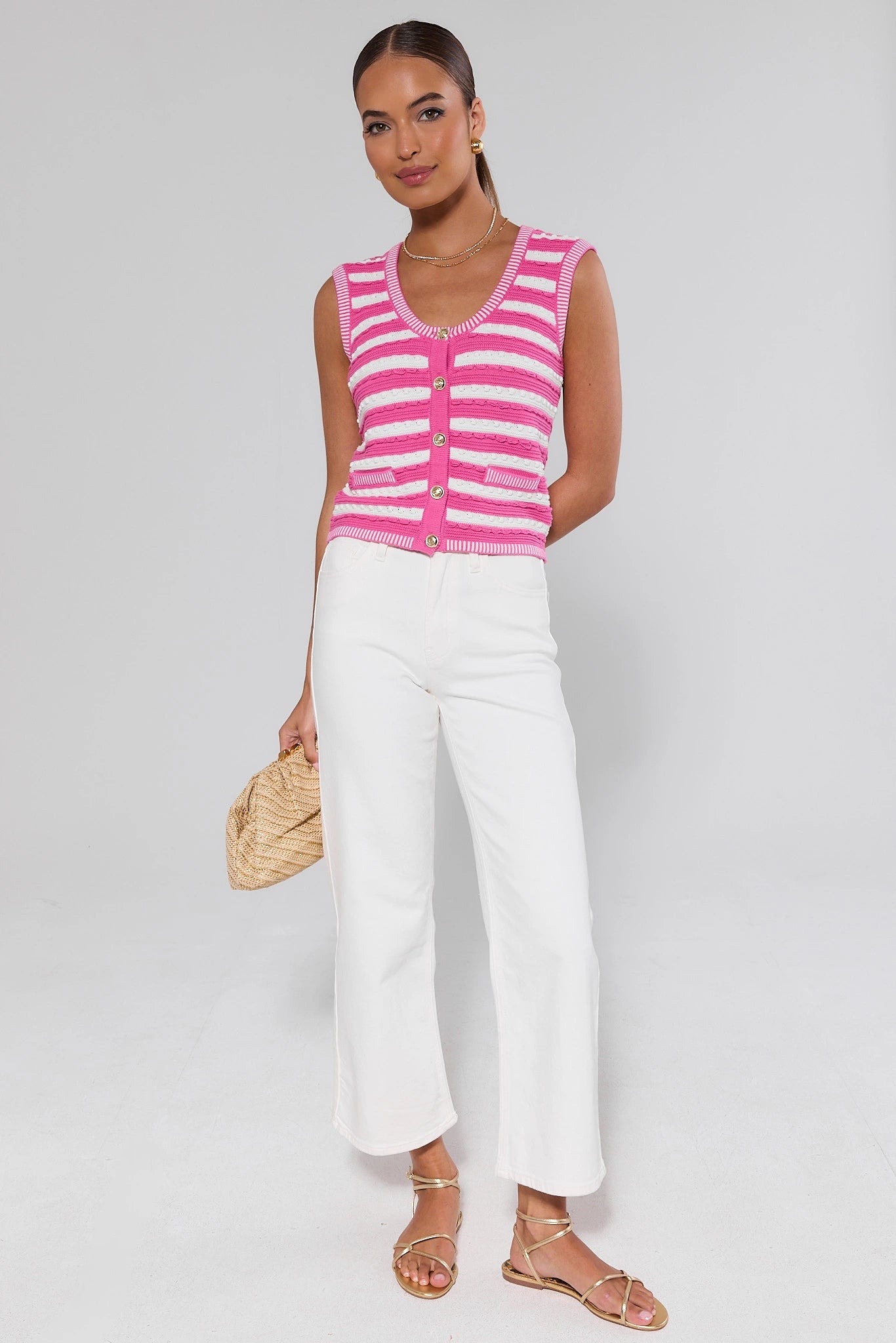 Woman wearing a pink and white striped cardigan with white pants on a plain background
