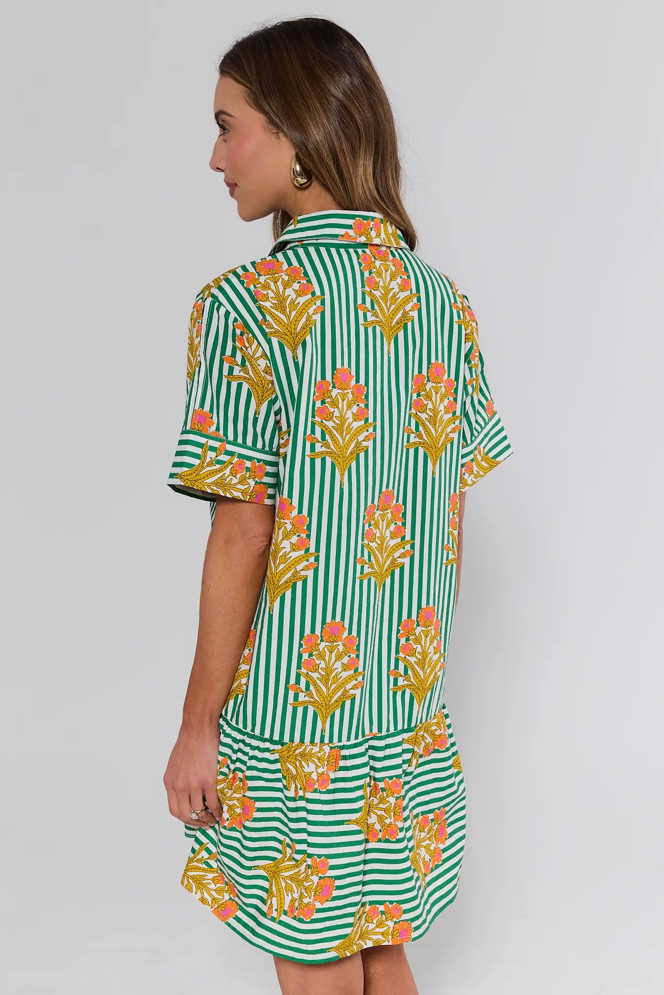 Woman standing wearing a green and white striped dress with floral patterns on a plain background