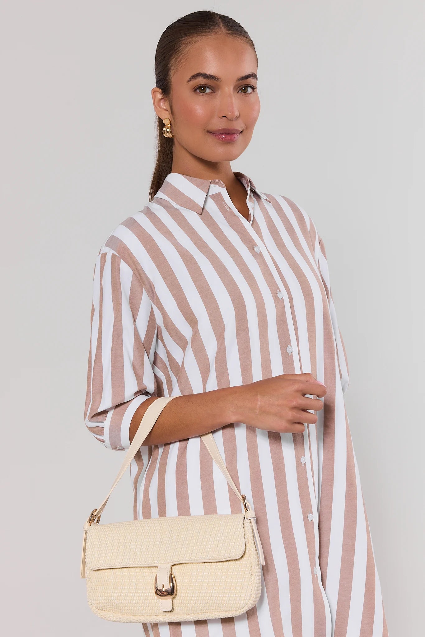 Woman wearing a striped dress holding a beige handbag against a plain background