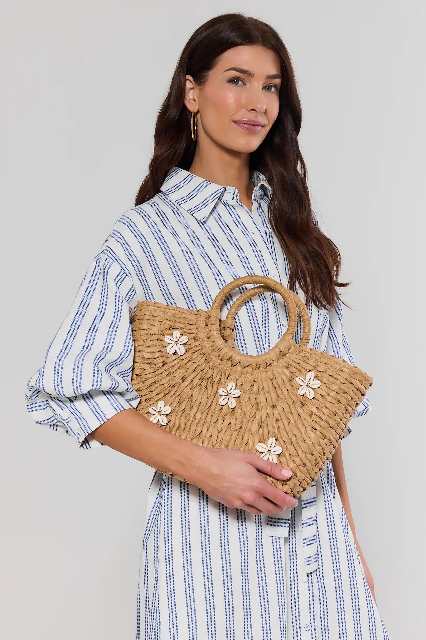 Woman holding a woven handbag with floral embellishments against a plain background