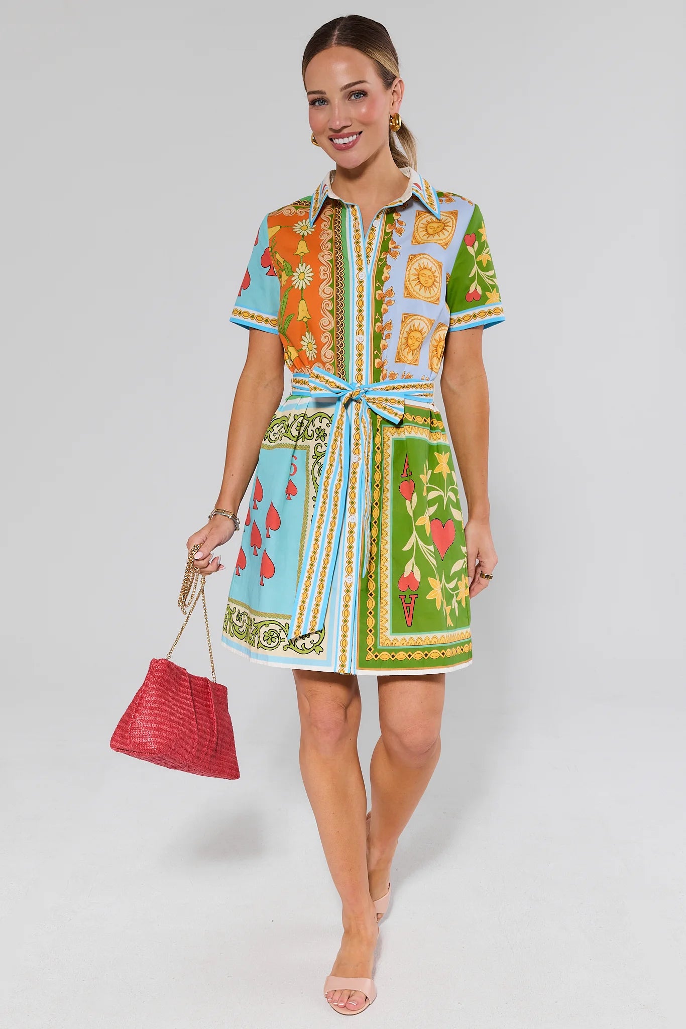 Woman wearing a colorful patterned dress holding a red handbag on a white background