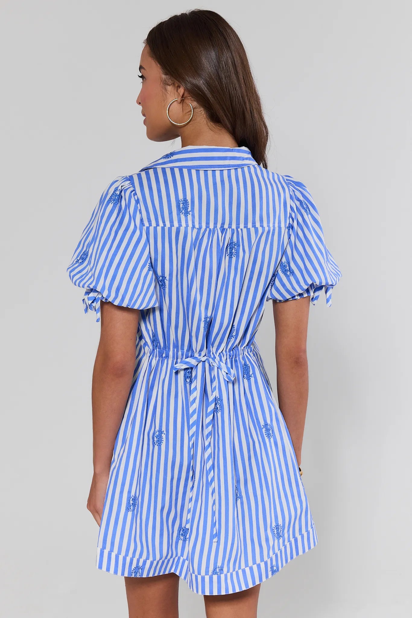 Woman standing wearing a blue and white striped dress against a gray background
