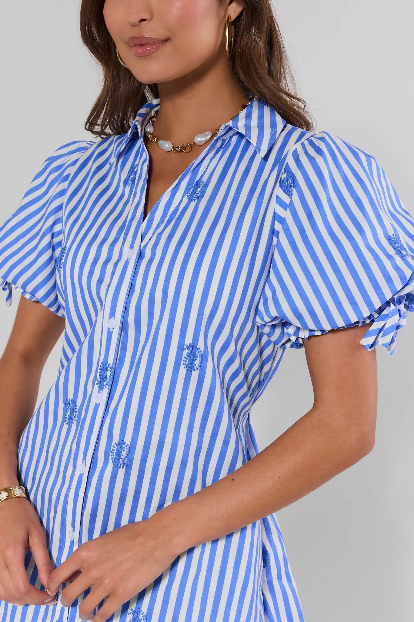 close up Woman wearing a blue and white striped dress with floral embroidery on a gray background