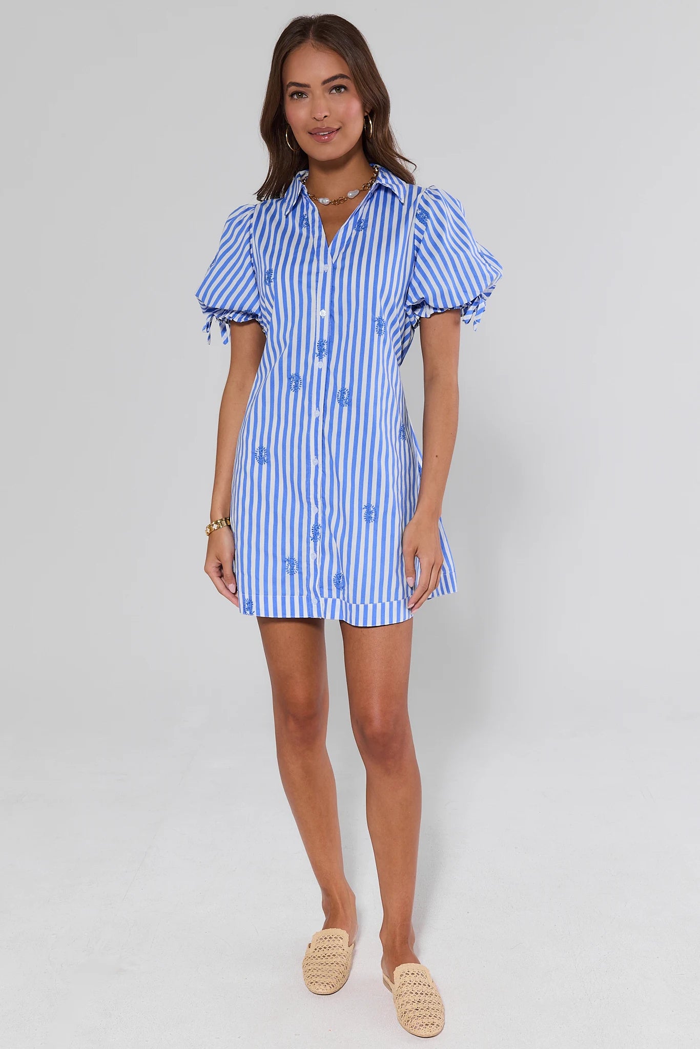 Woman wearing a blue and white striped dress and mules on a plain background
