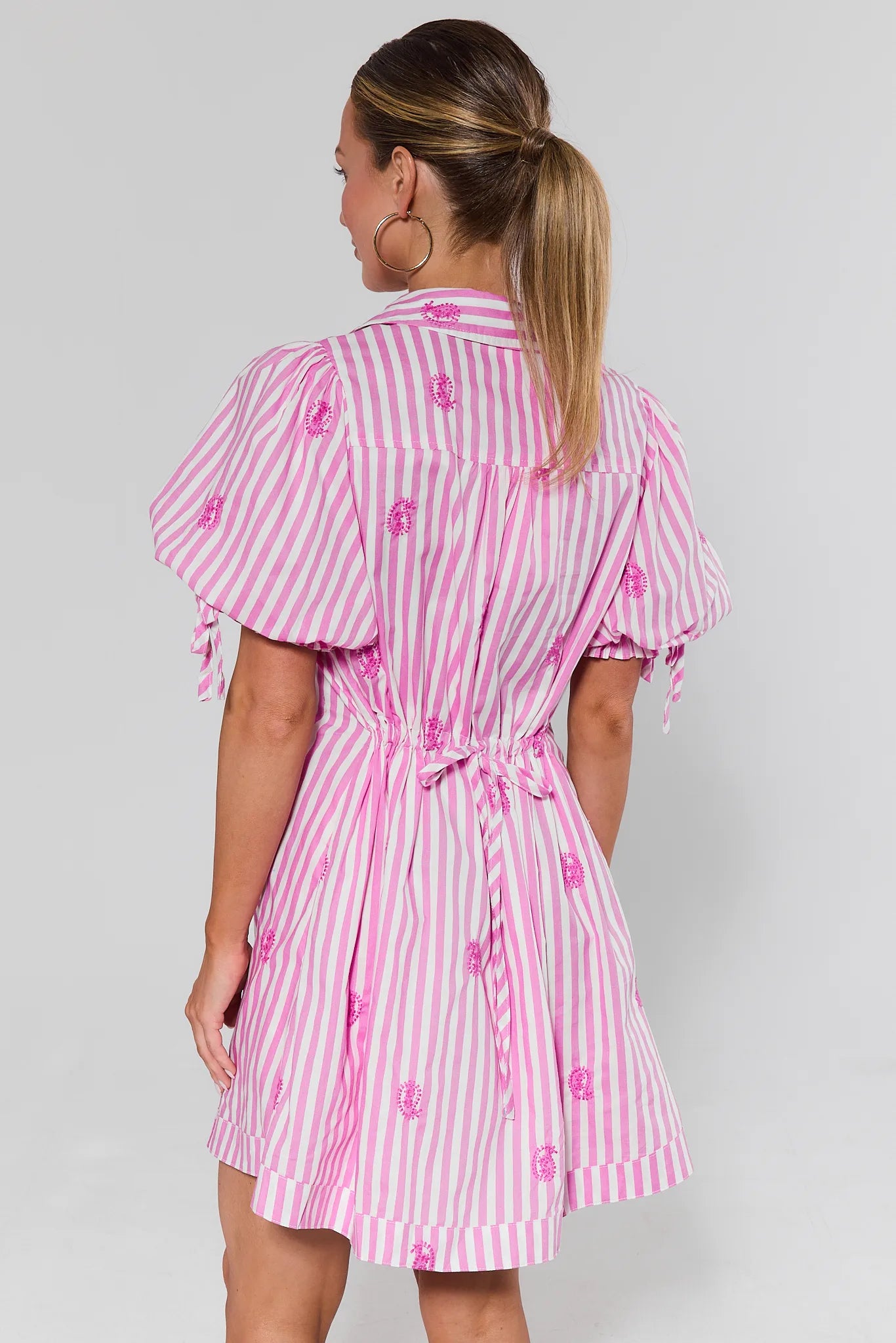 Woman standing wearing a pink and white striped dress with floral details on a gray background