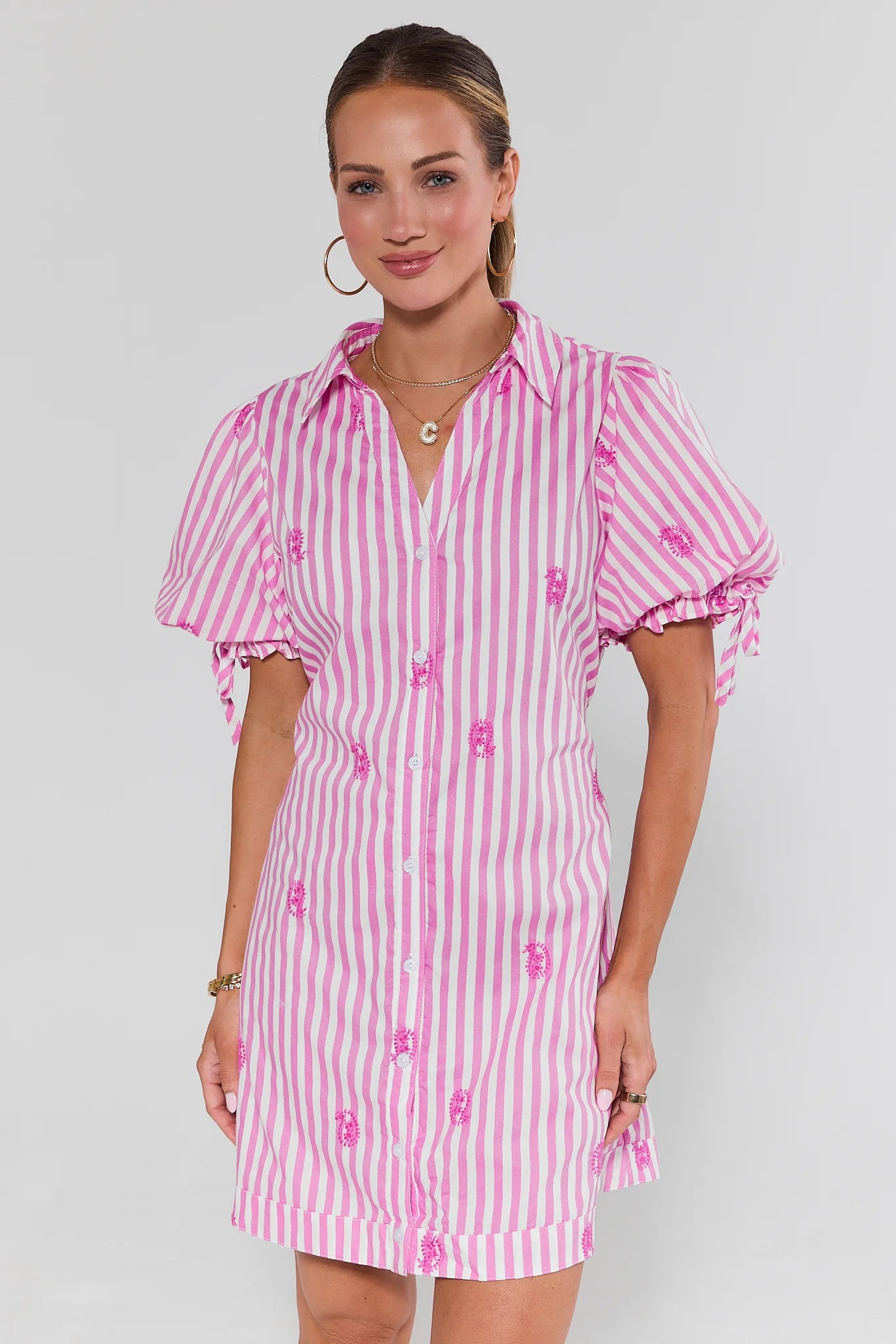 Woman wearing a pink and white striped dress with puff sleeves on a plain background