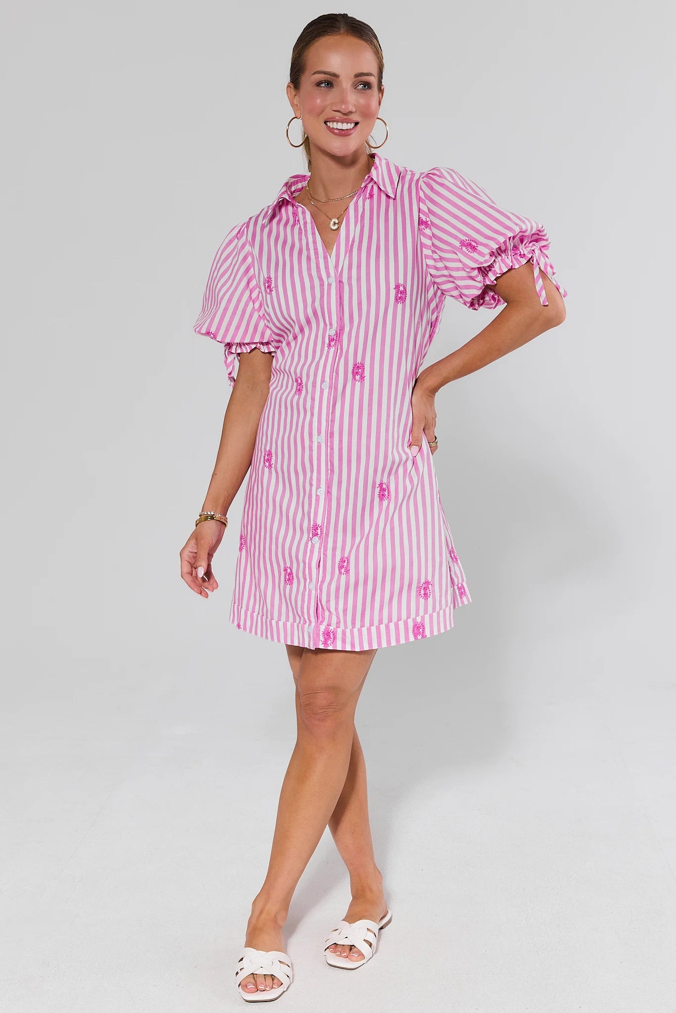 Woman wearing a pink and white striped dress with puff sleeves on a gray background