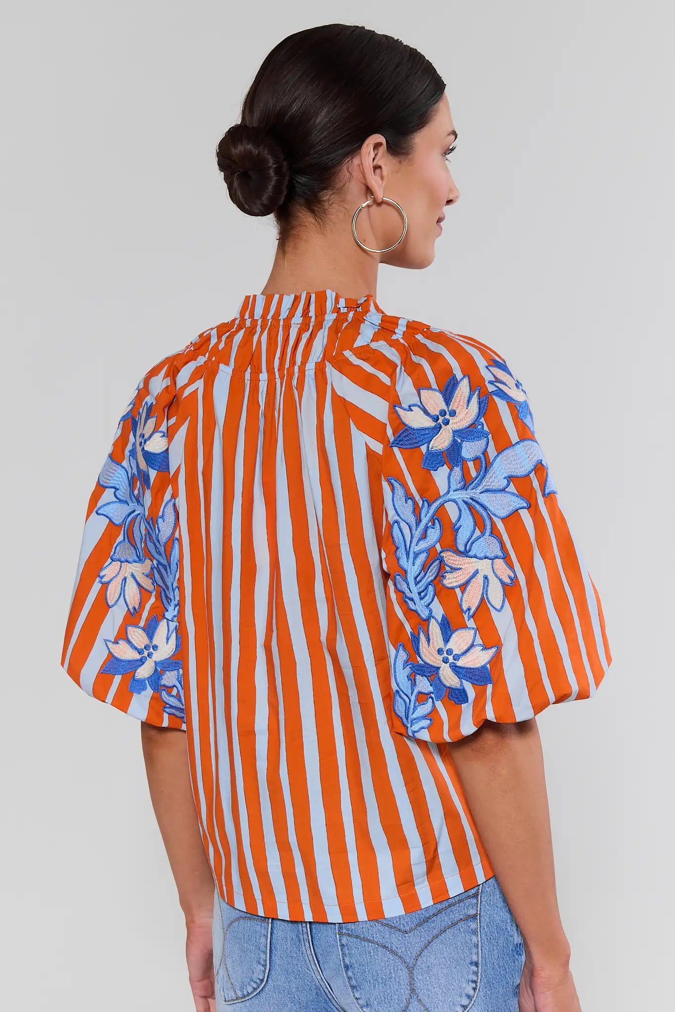 Woman standing wearing an orange and white striped shirt with blue floral patterns on a plain background