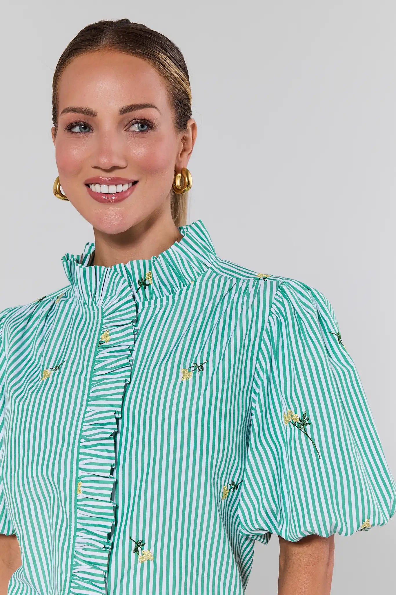 close up Woman wearing a green and white striped blouse with floral embroidery on a gray background
