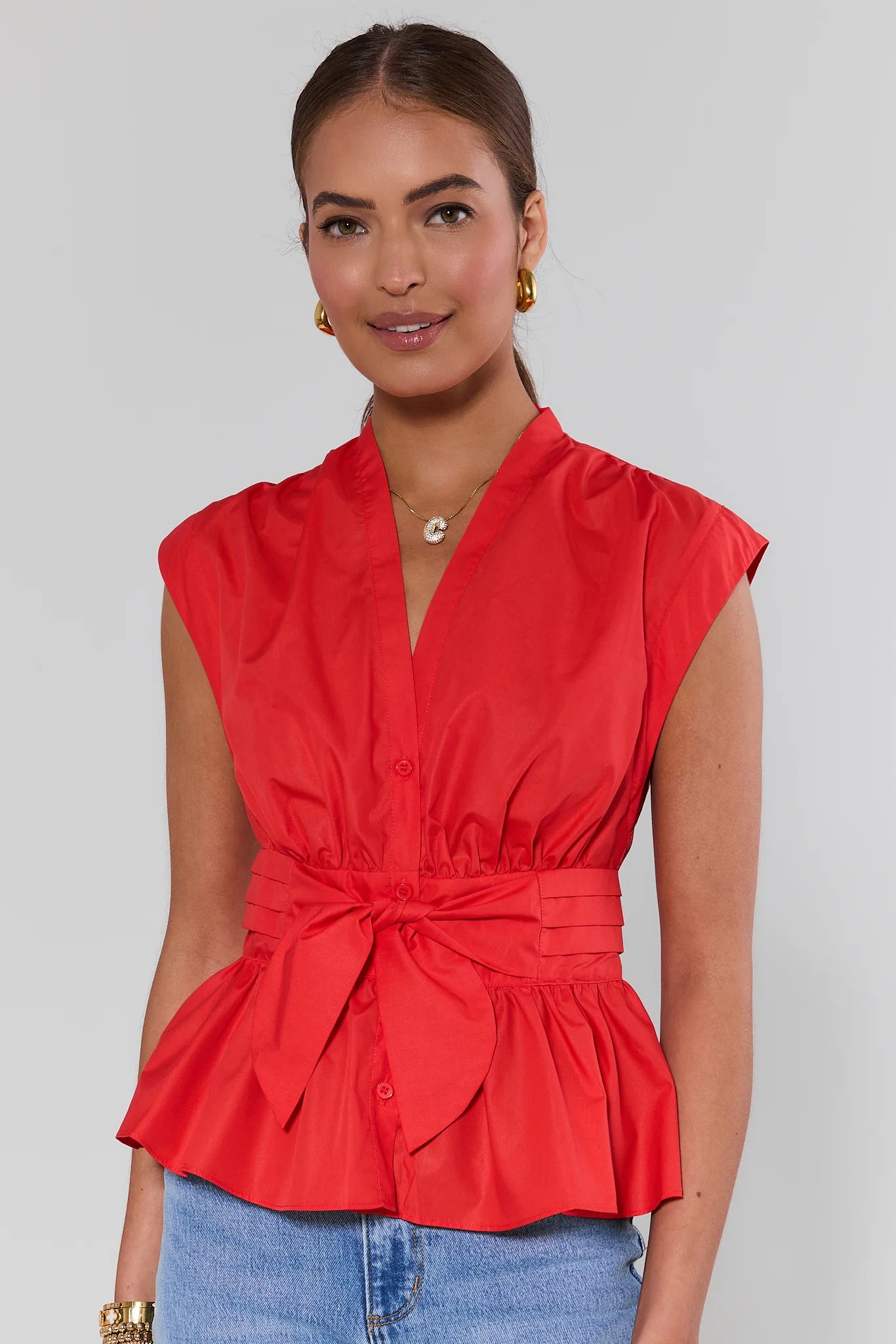 Woman wearing a red sleeveless blouse with a tie waist against a plain background