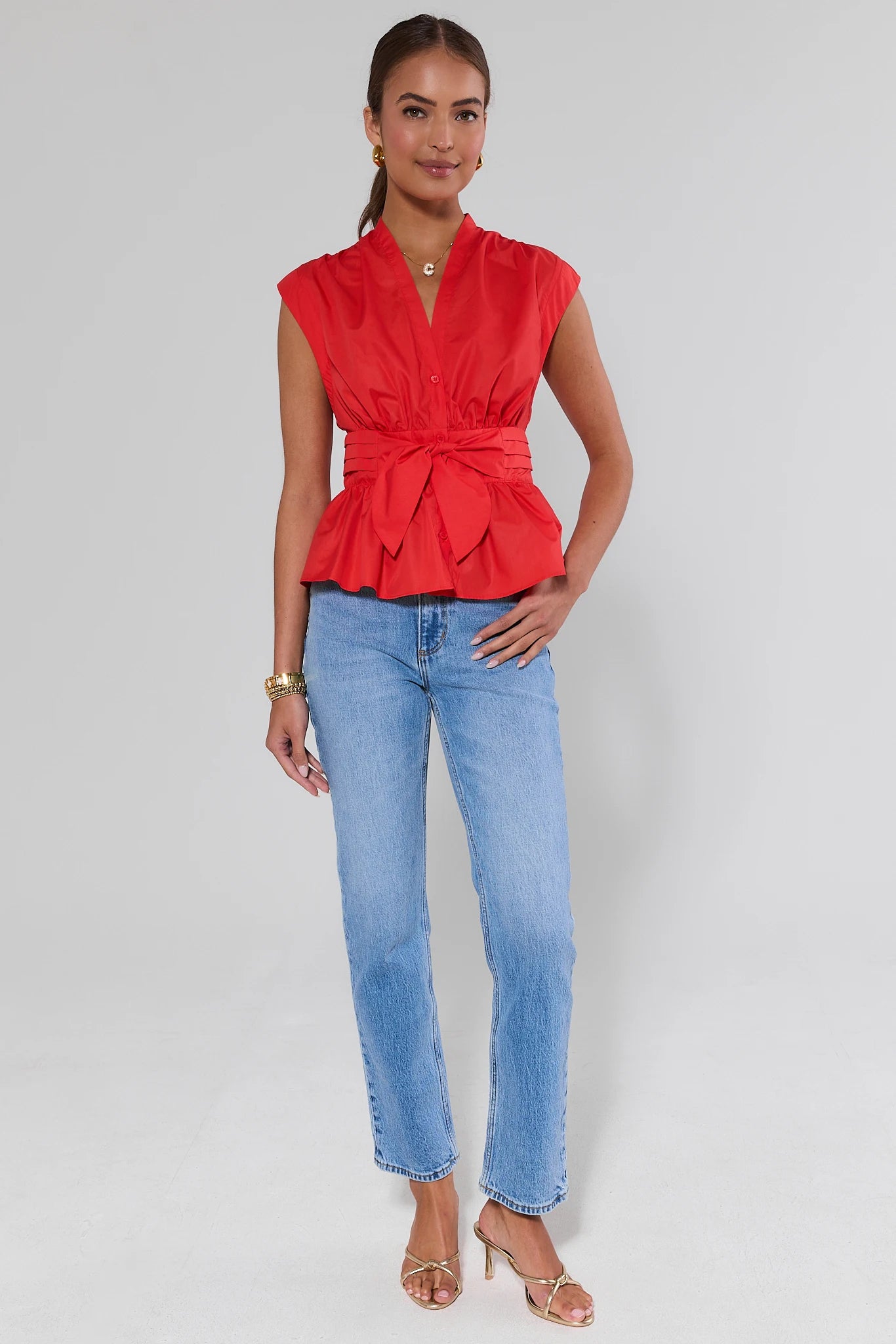 Woman wearing a red sleeveless top and blue jeans on a gray background