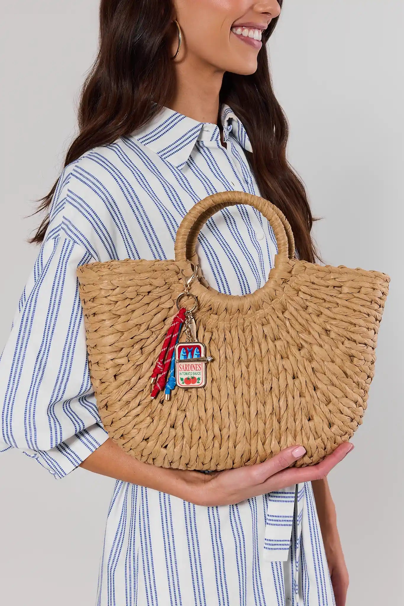 Woman holding a woven handbag with a decorative charm against a neutral background