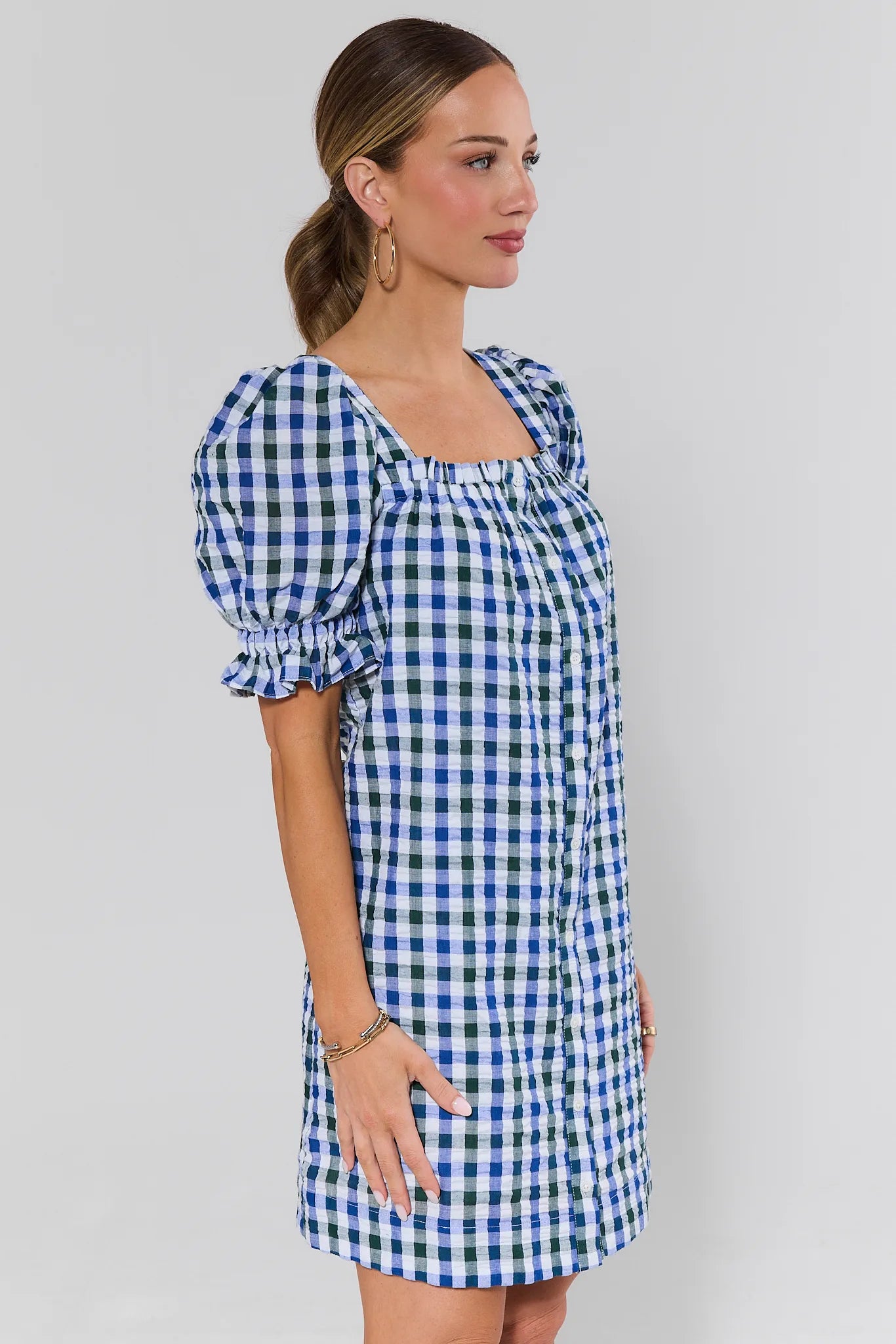 side shot Woman wearing a blue and white checkered dress against a plain background