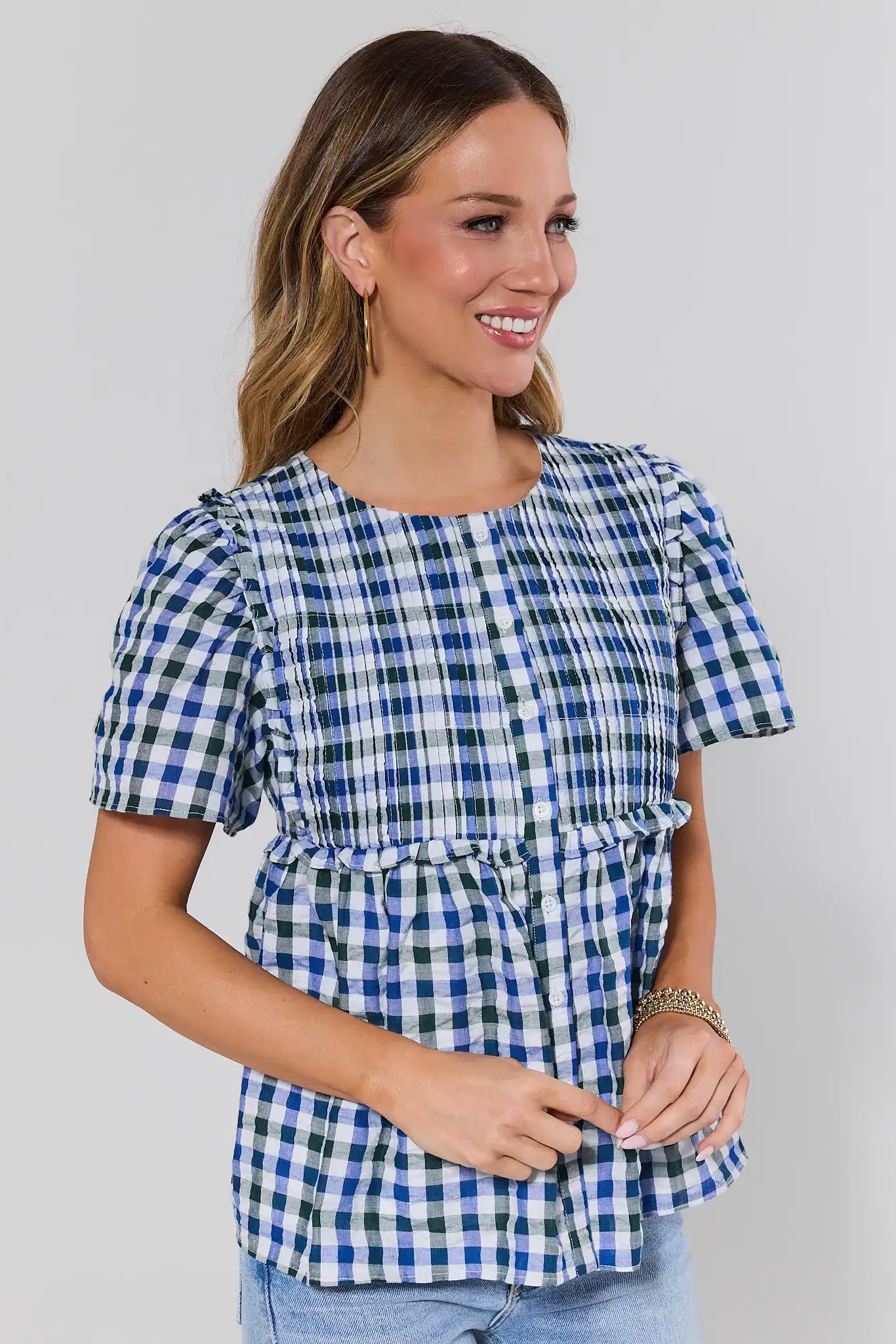side shot Woman wearing a blue and white checkered top with puff sleeves on a gray background