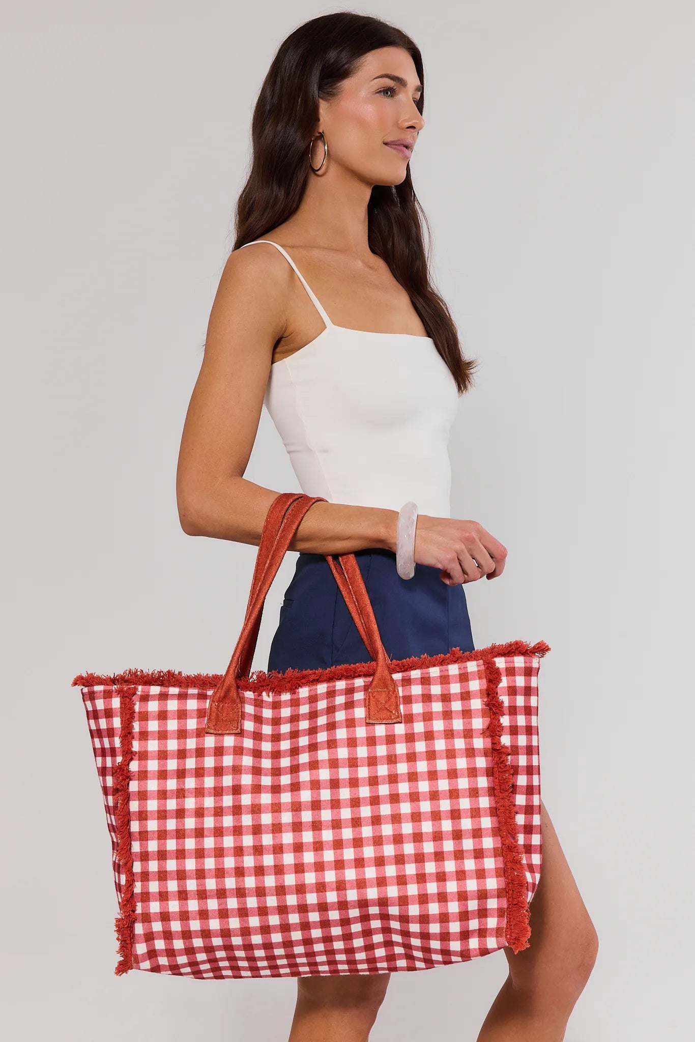 Woman holding a red and white checkered bag against a plain background