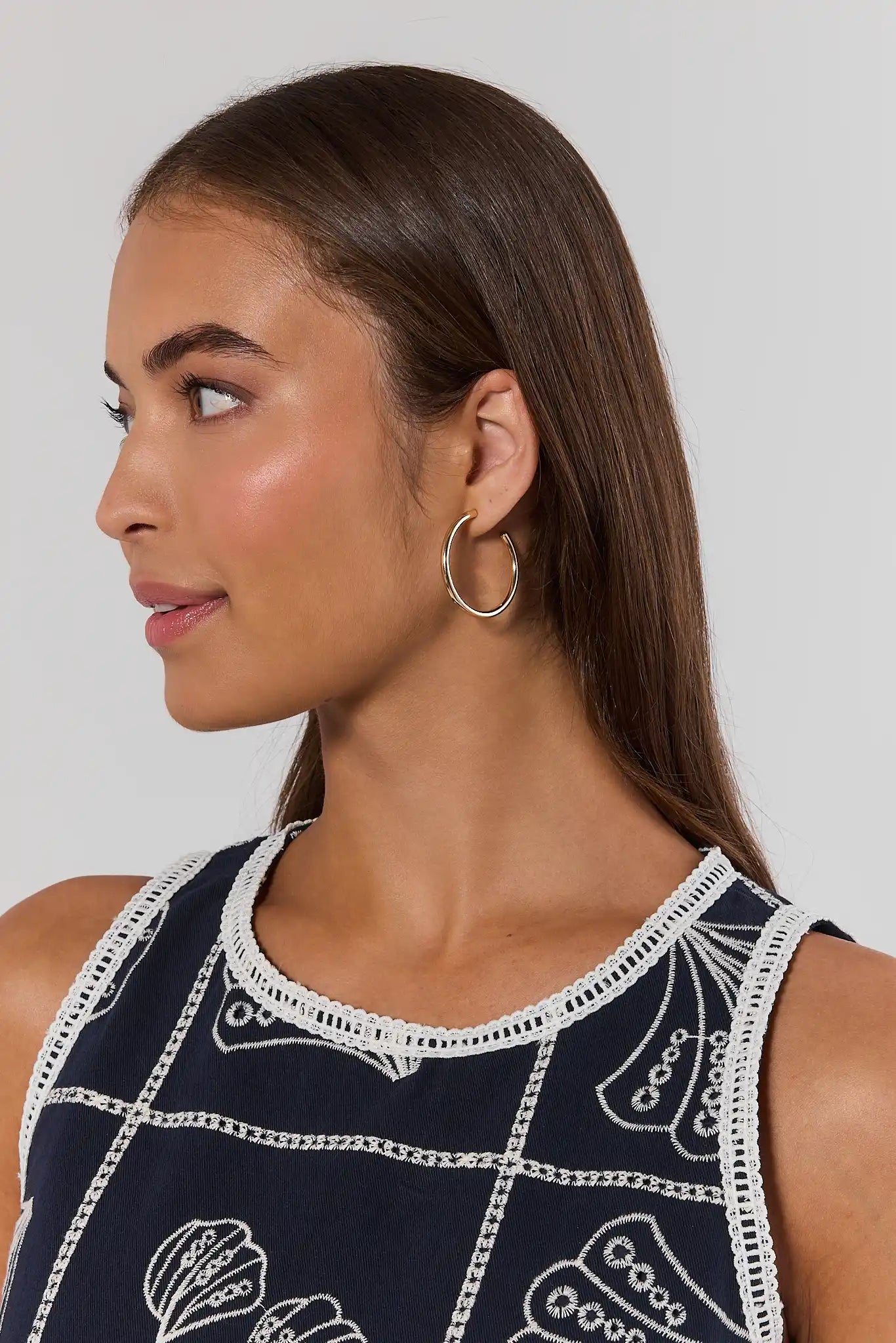 Woman wearing a sleeveless top with intricate patterns and hoop earrings against a plain background