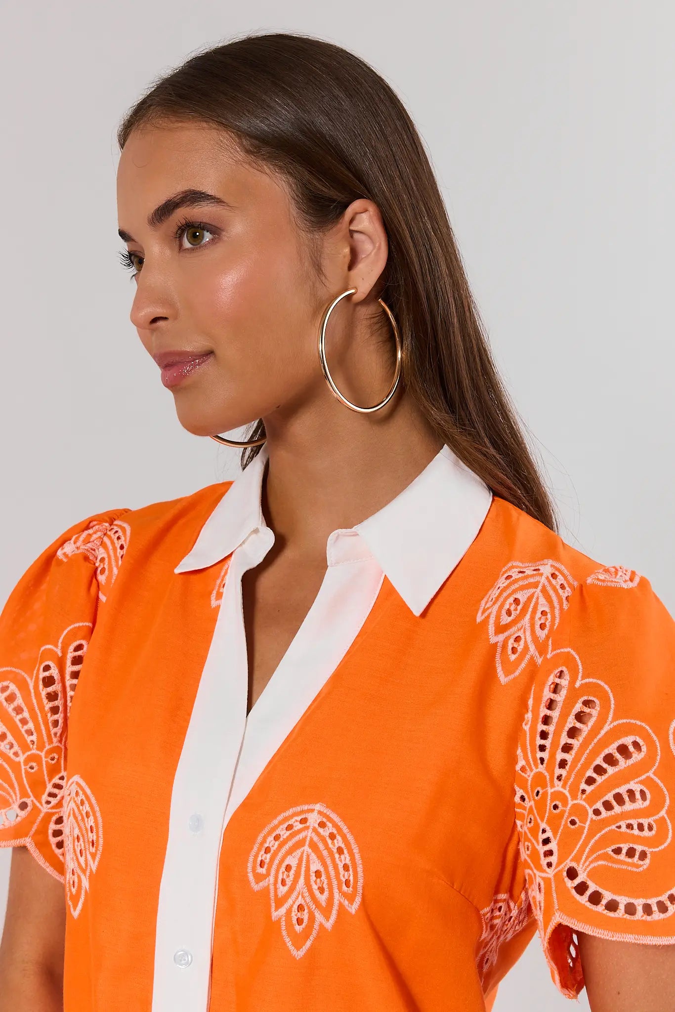 Woman wearing an orange patterned blouse with a white collar against a plain background