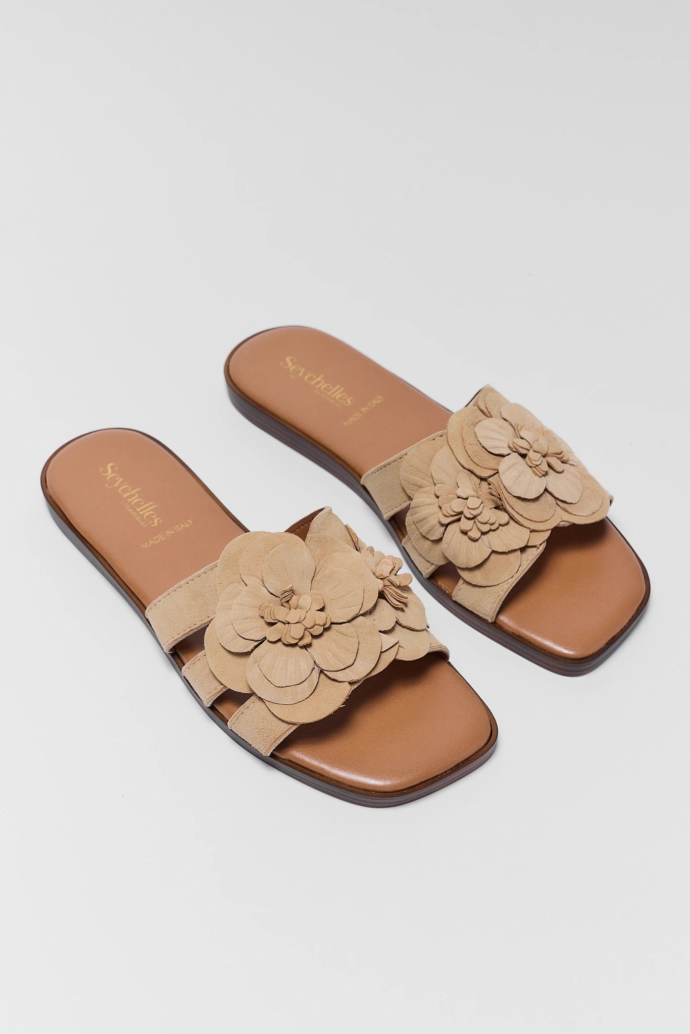 Pair of beige sandals with floral details on a light gray background two