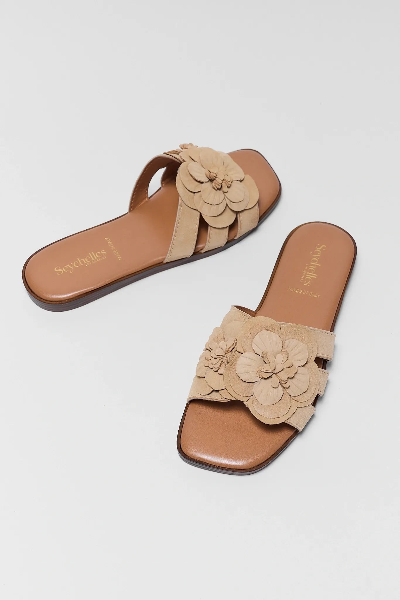 Pair of beige sandals with floral designs on a light gray background