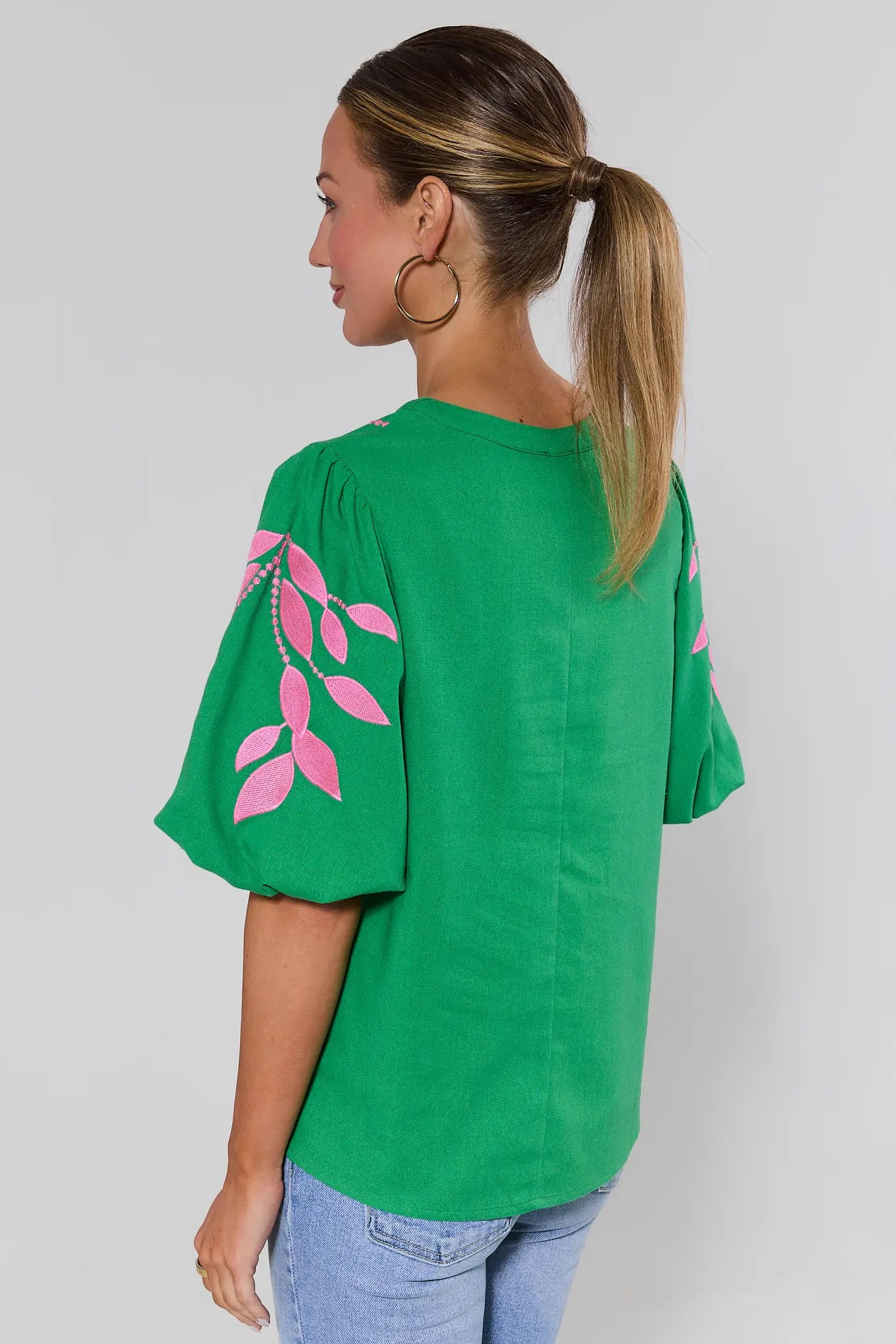 Woman standing wearing a green t-shirt with pink leaf design on a plain background