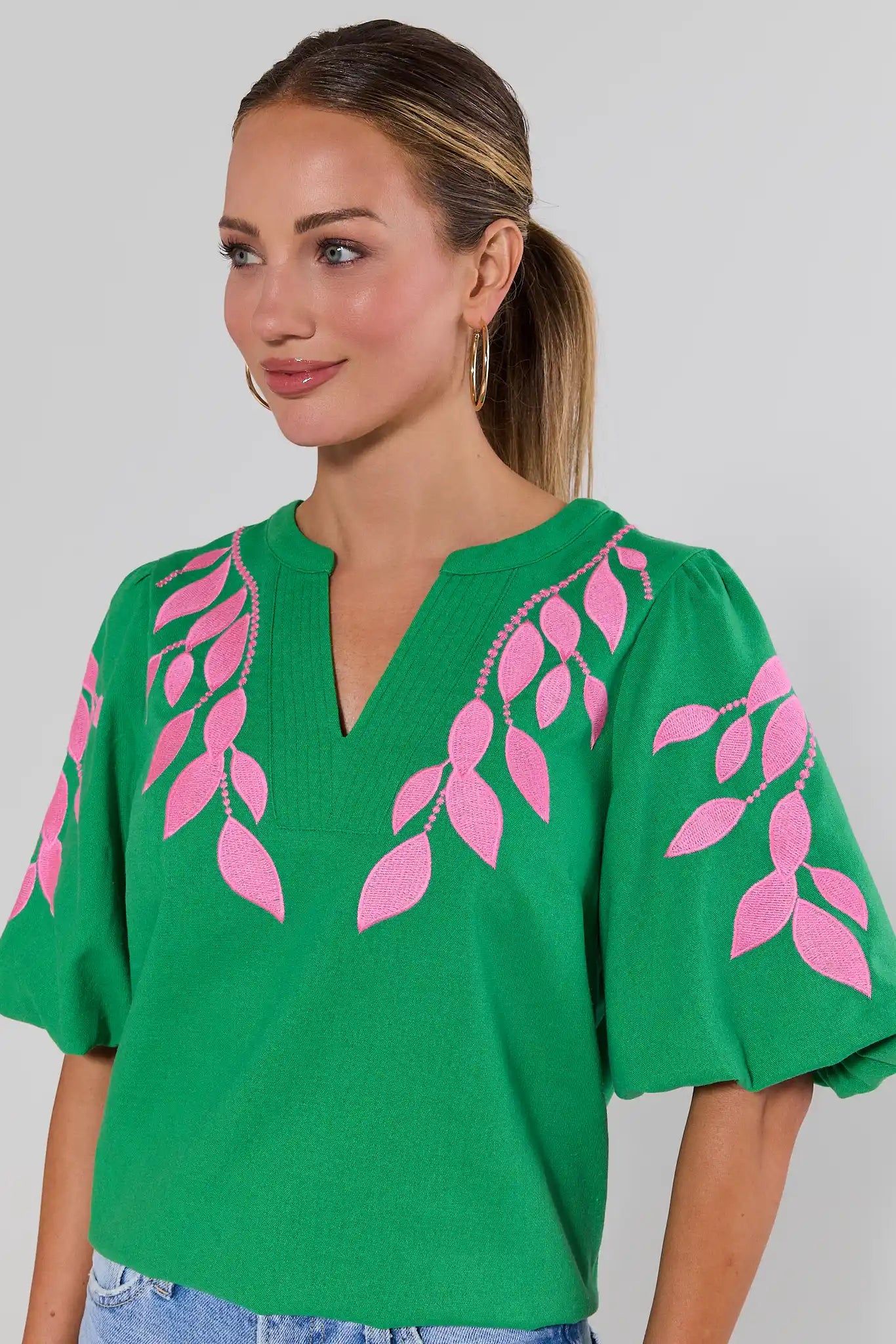close up Woman wearing a green top with pink leaf patterns on a plain background