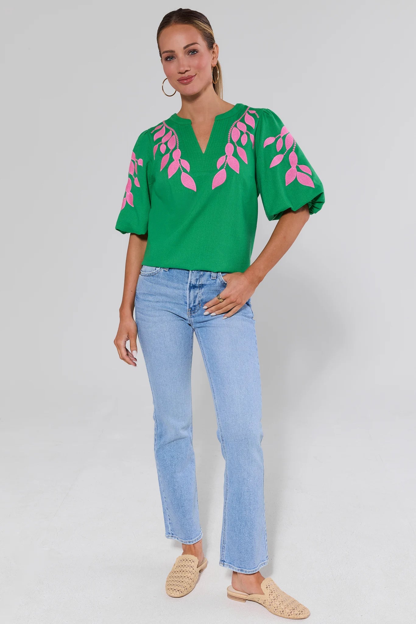 Woman wearing a green blouse with pink leaf patterns and light blue jeans on a gray background