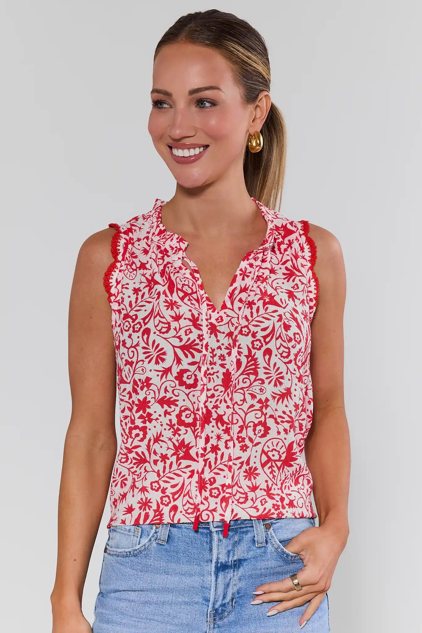 Woman wearing a red and white floral sleeveless top with blue jeans on a plain background