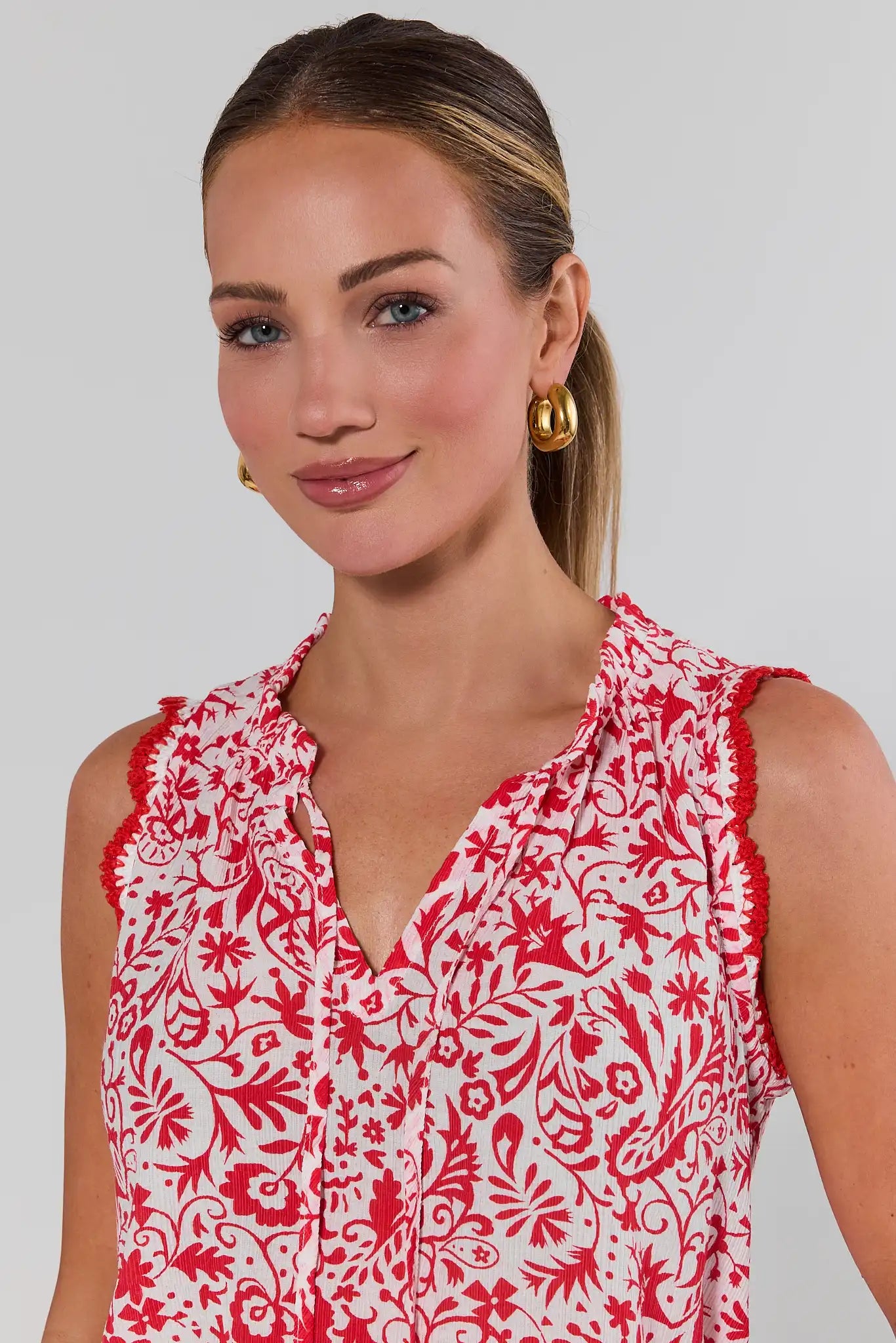 close up Woman wearing a red and white patterned sleeveless top against a plain background