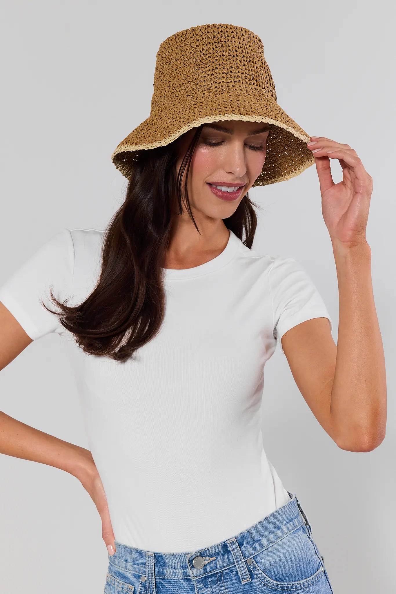 Woman wearing a beige bucket hat, white t-shirt, and blue jeans on a gray background