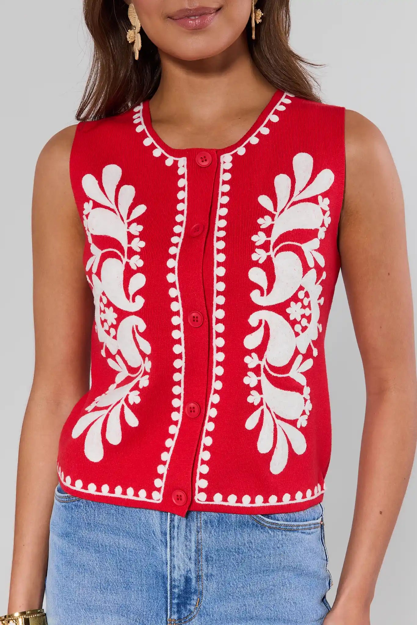 close up Red sleeveless top with white floral embroidery worn by a person on a plain background