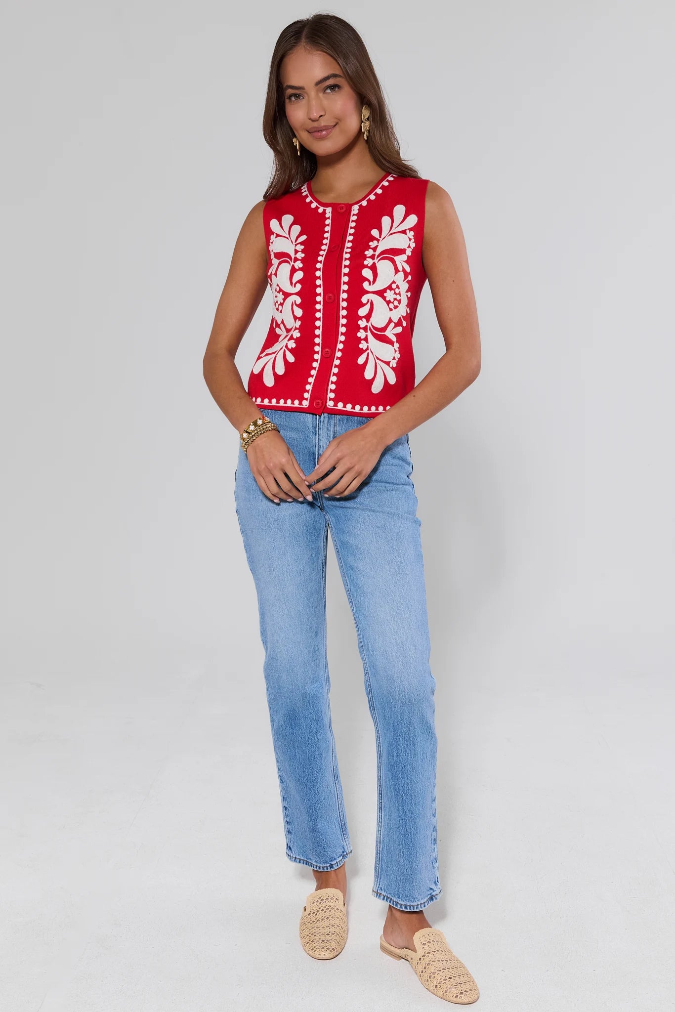 Woman wearing a red sleeveless top with white patterns and blue jeans on a light gray background