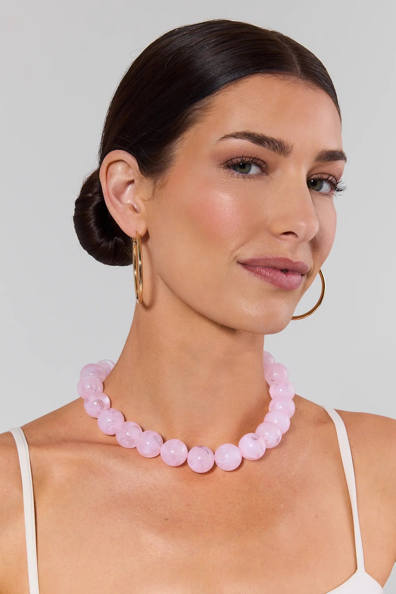 Woman wearing a pink beaded necklace and hoop earrings on a plain background