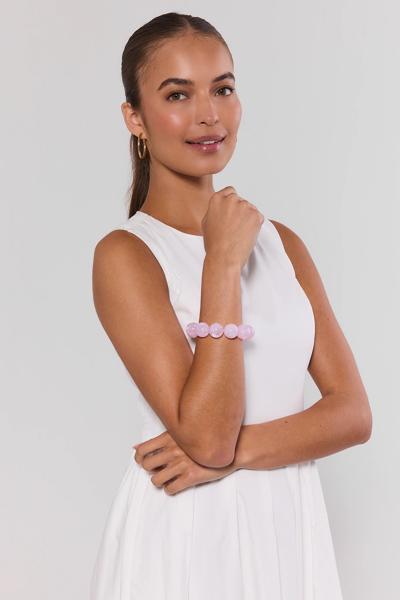 Woman wearing a white sleeveless top and pink bracelet on a plain background