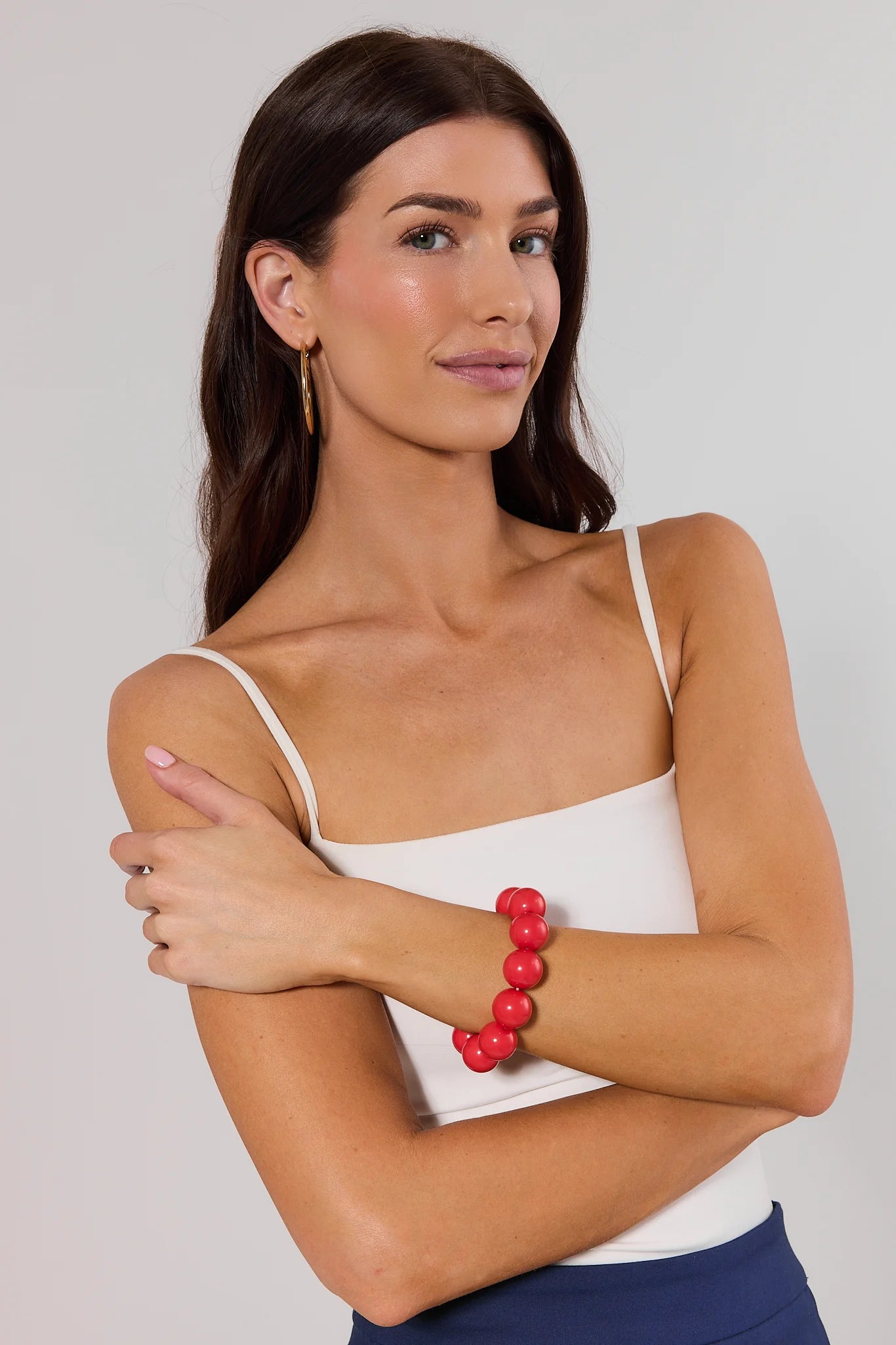 Woman wearing a white tank top and red beaded bracelet on a plain background