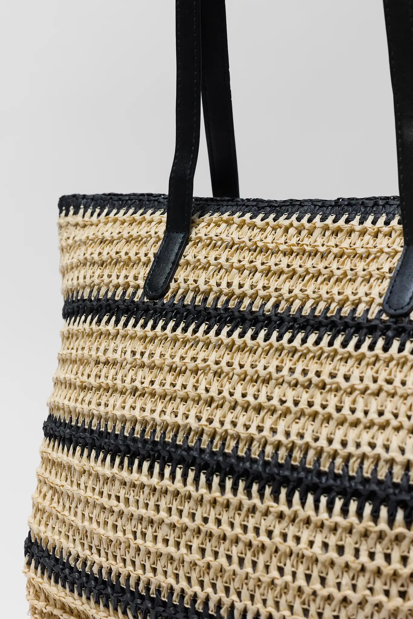 close up Woven straw bag with black accents on a light gray background