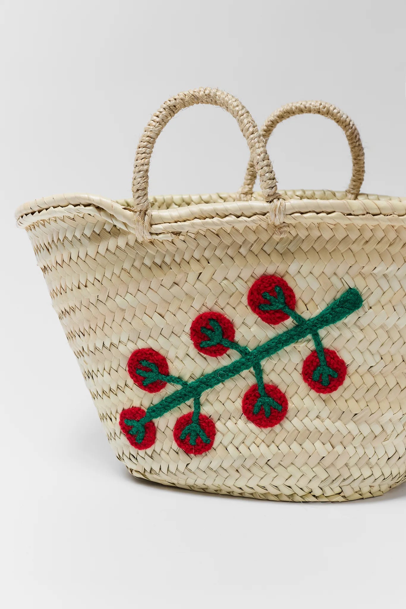 close up Woven basket with embroidered red flowers and green leaves on a light gray background