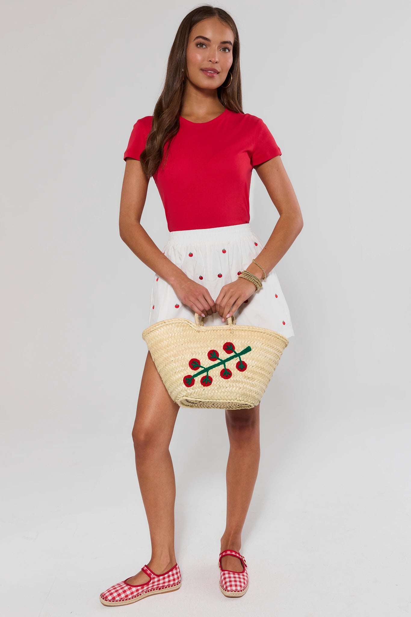 Woman holding a straw bag with cherry design against a plain background