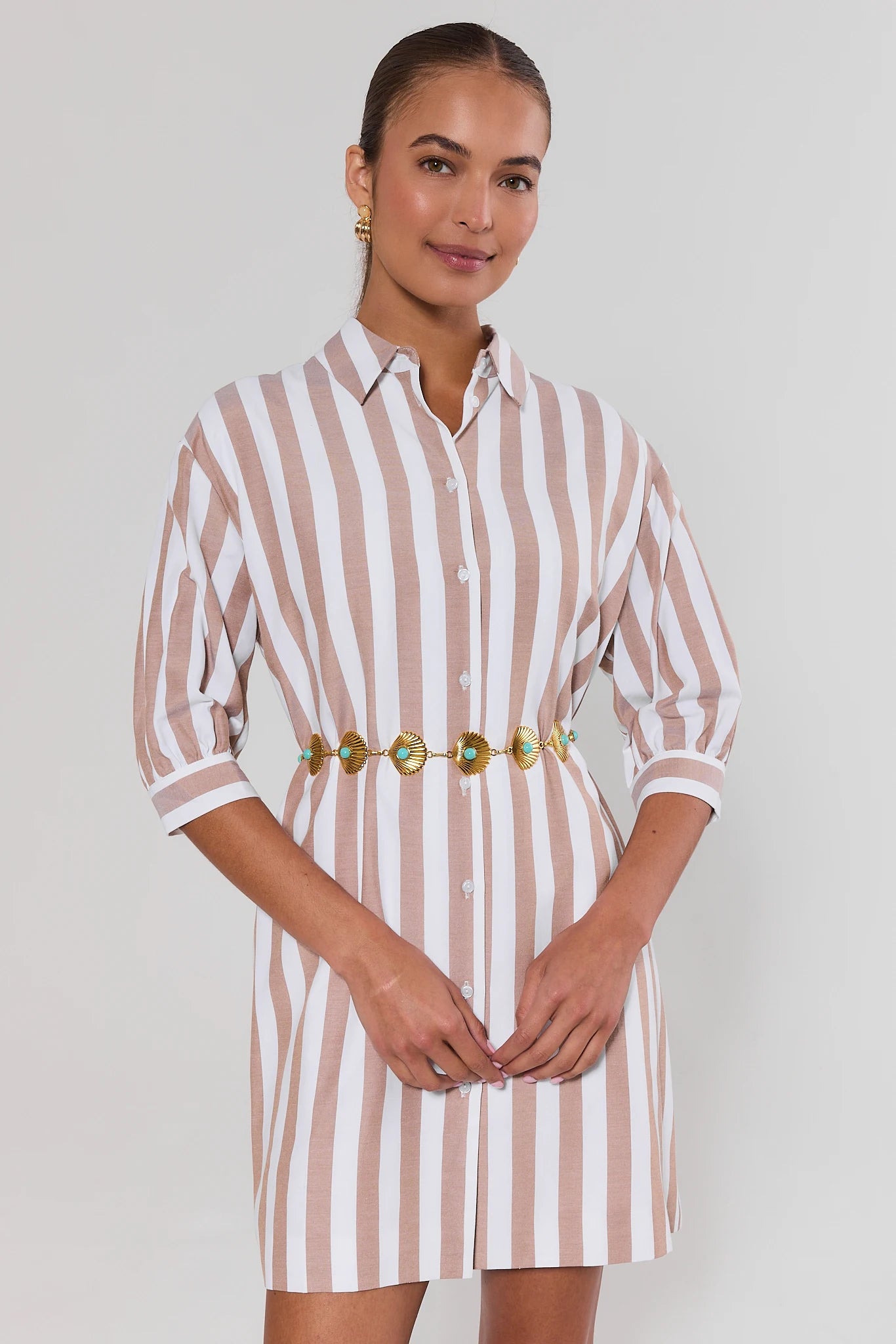 Woman wearing a striped dress with a gold belt against a plain background