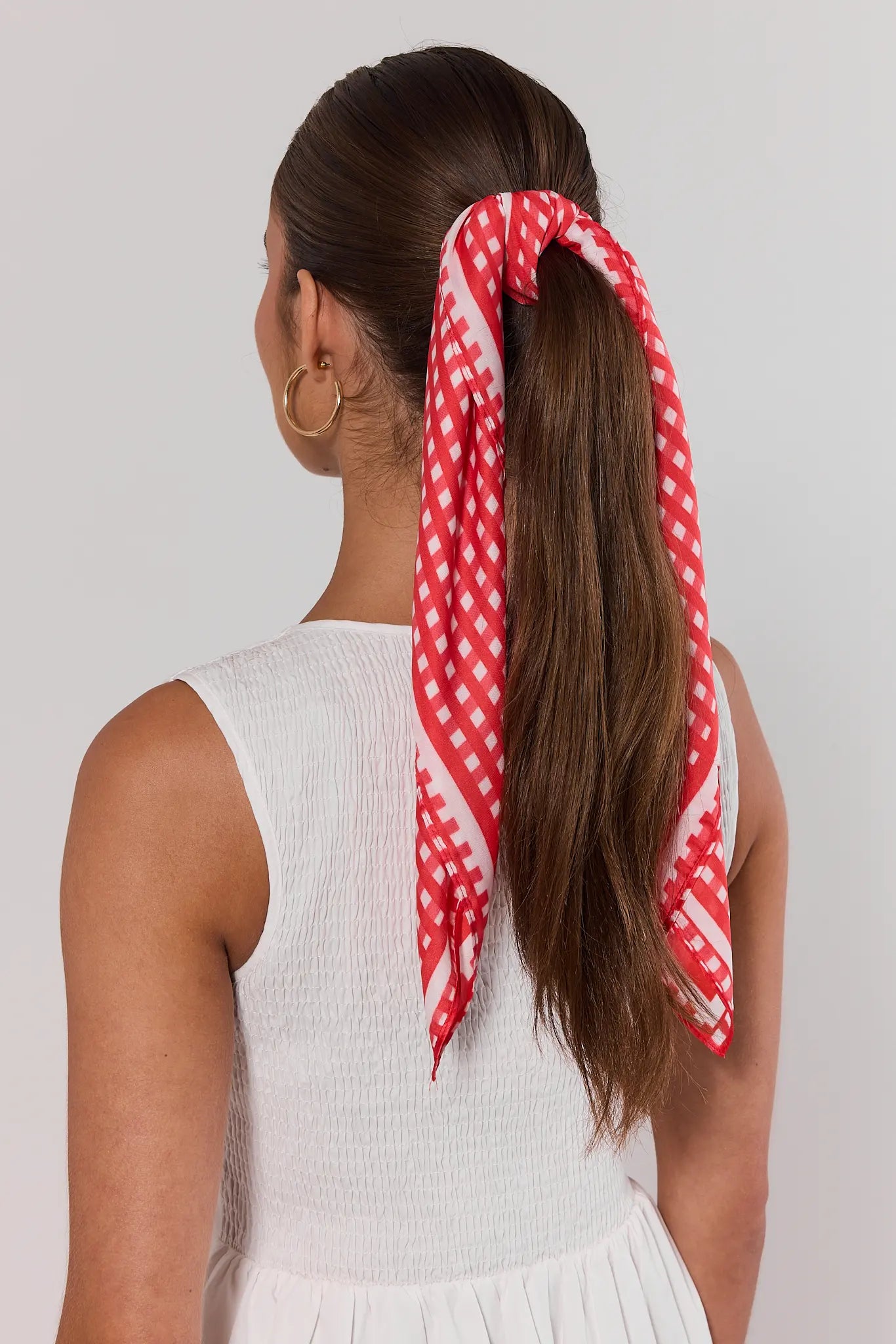 Woman with a red and white checkered scarf tied around her ponytail on a plain background