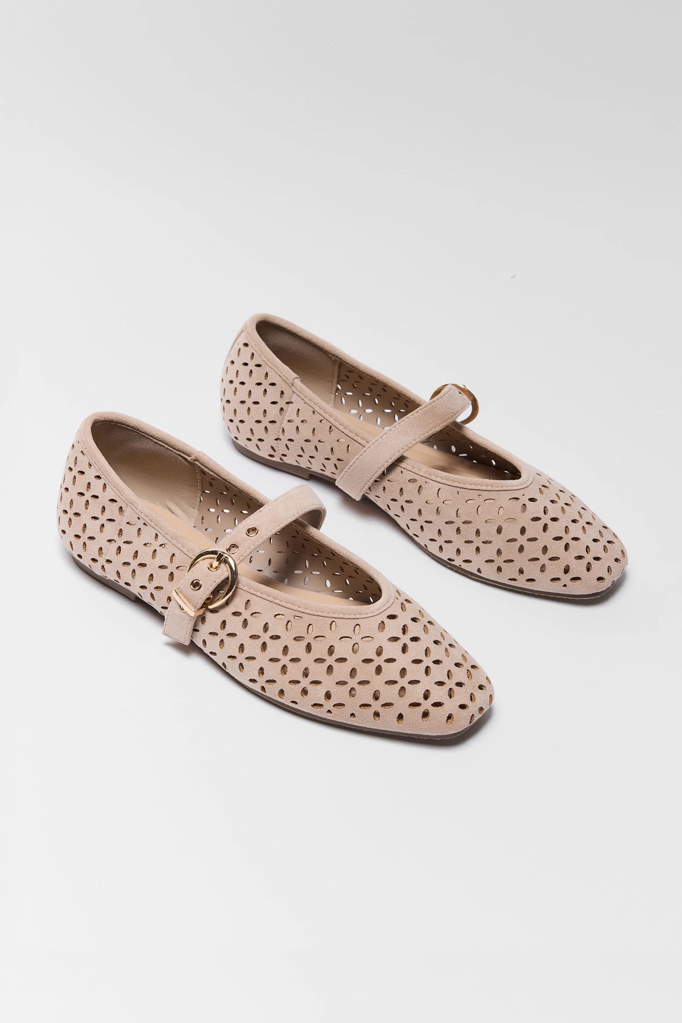 A pair of beige perforated leather Mary Jane flats with a small gold buckle, displayed on a light gray background.