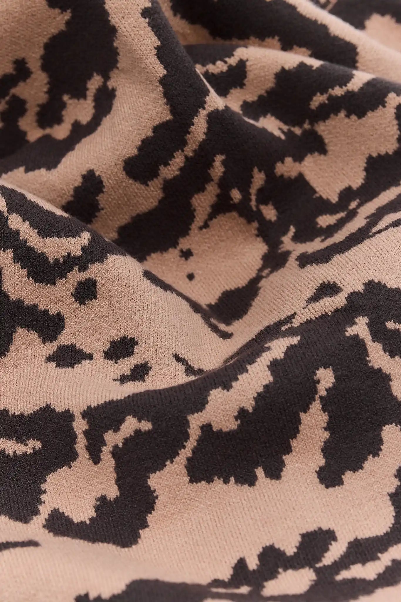 Close-up of a knit fabric with an abstract leopard-like pattern in beige and black.