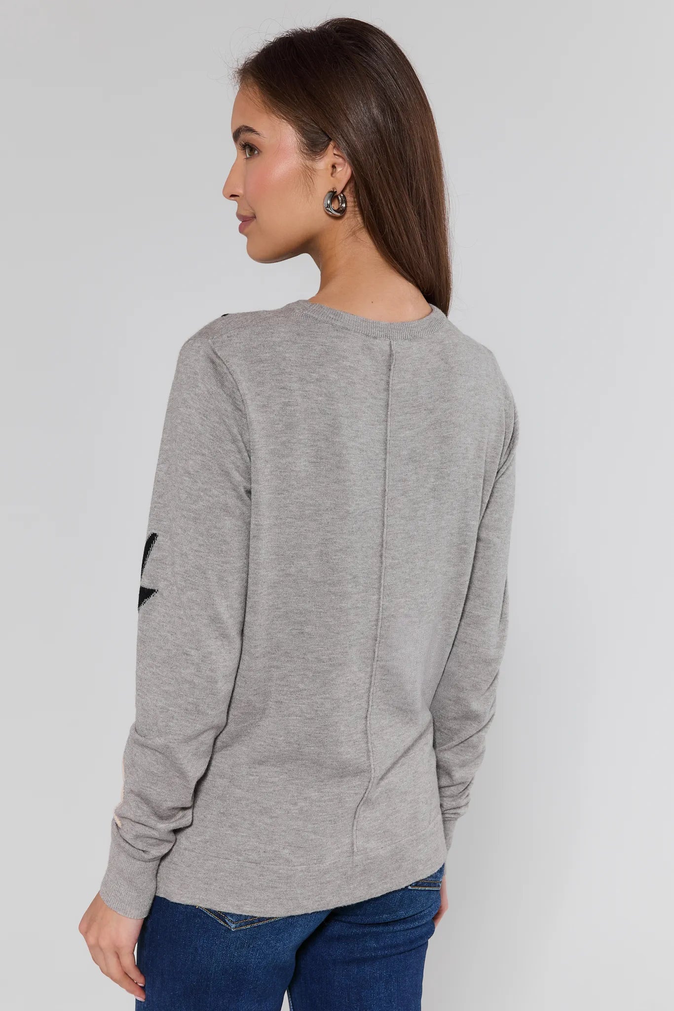 Woman wearing a gray long-sleeve top with a heart design on a plain background