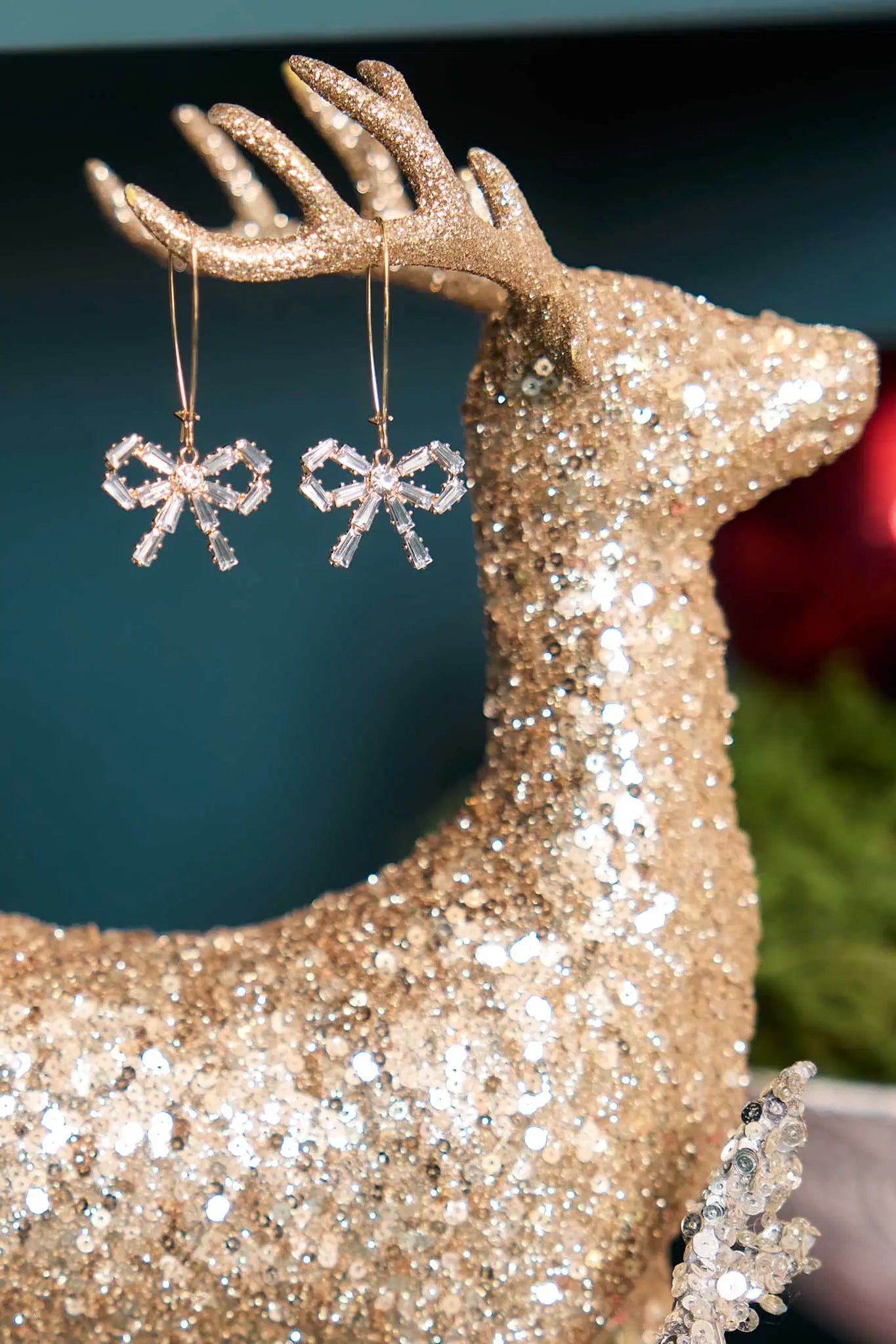 Gold glittery reindeer with diamond bow earrings hanging from its antlers against a dark background