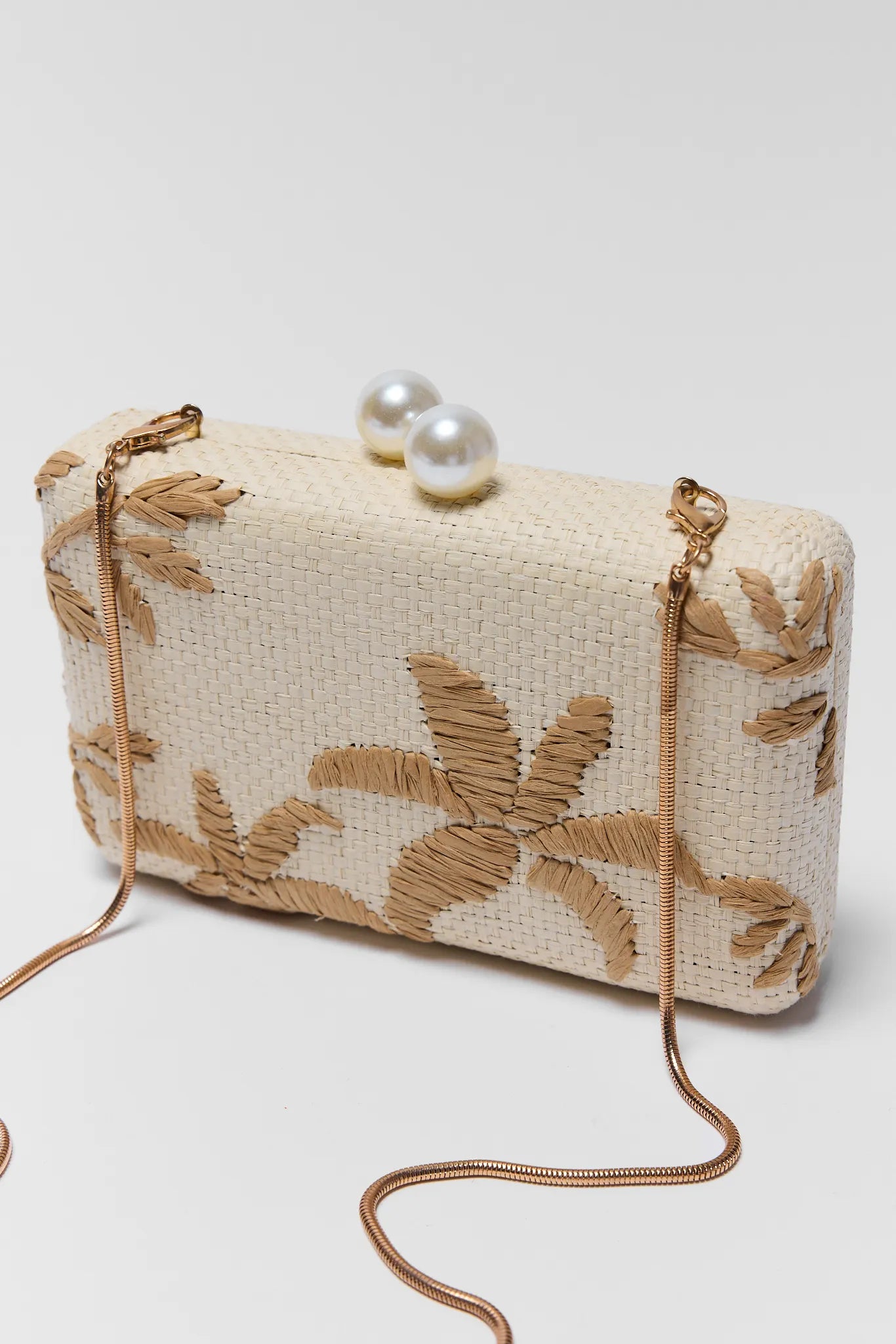 Beige clutch bag with floral embroidery and pearl embellishments on a white background