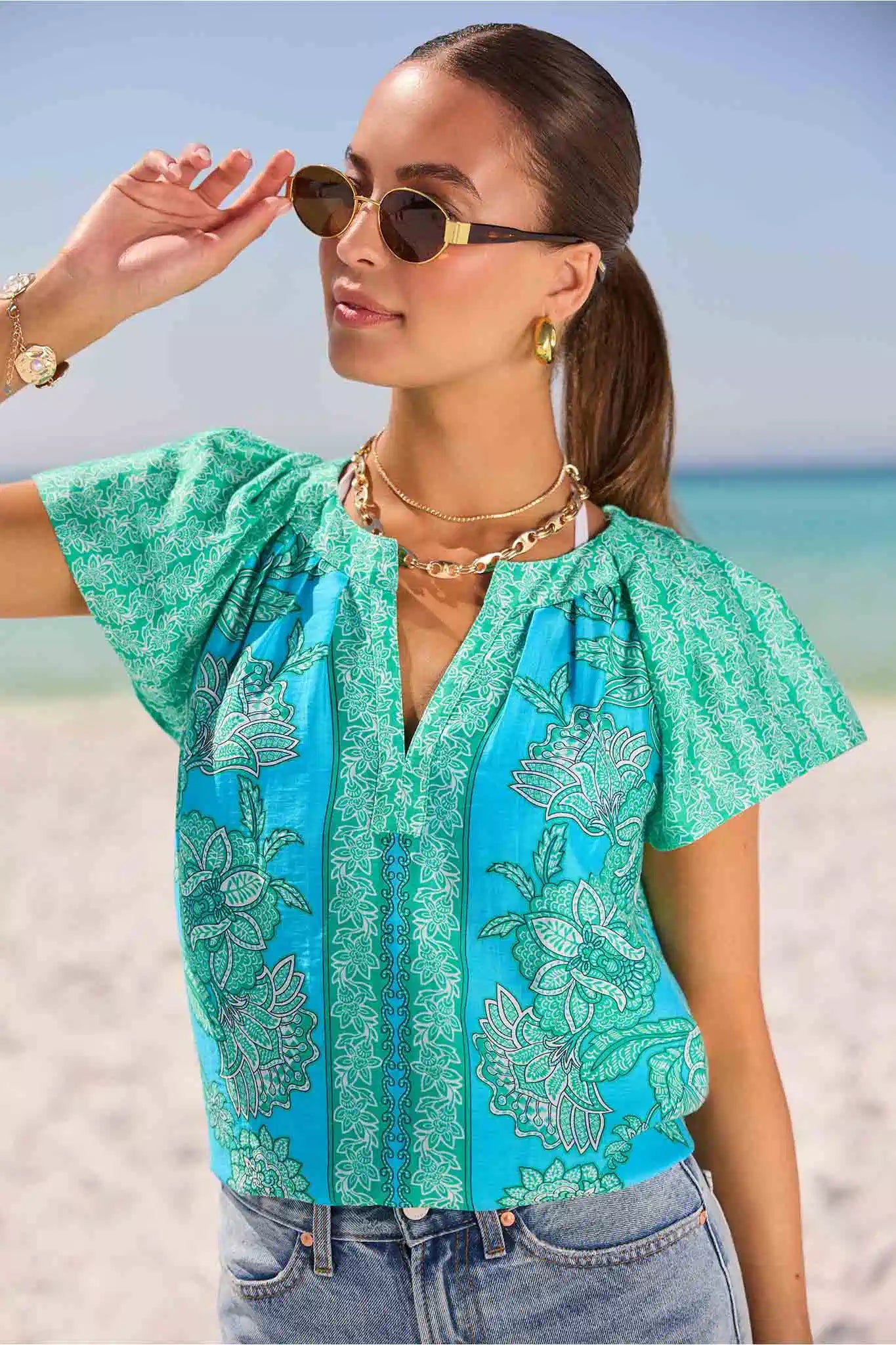 Woman wearing a turquoise blouse with floral patterns on a beach