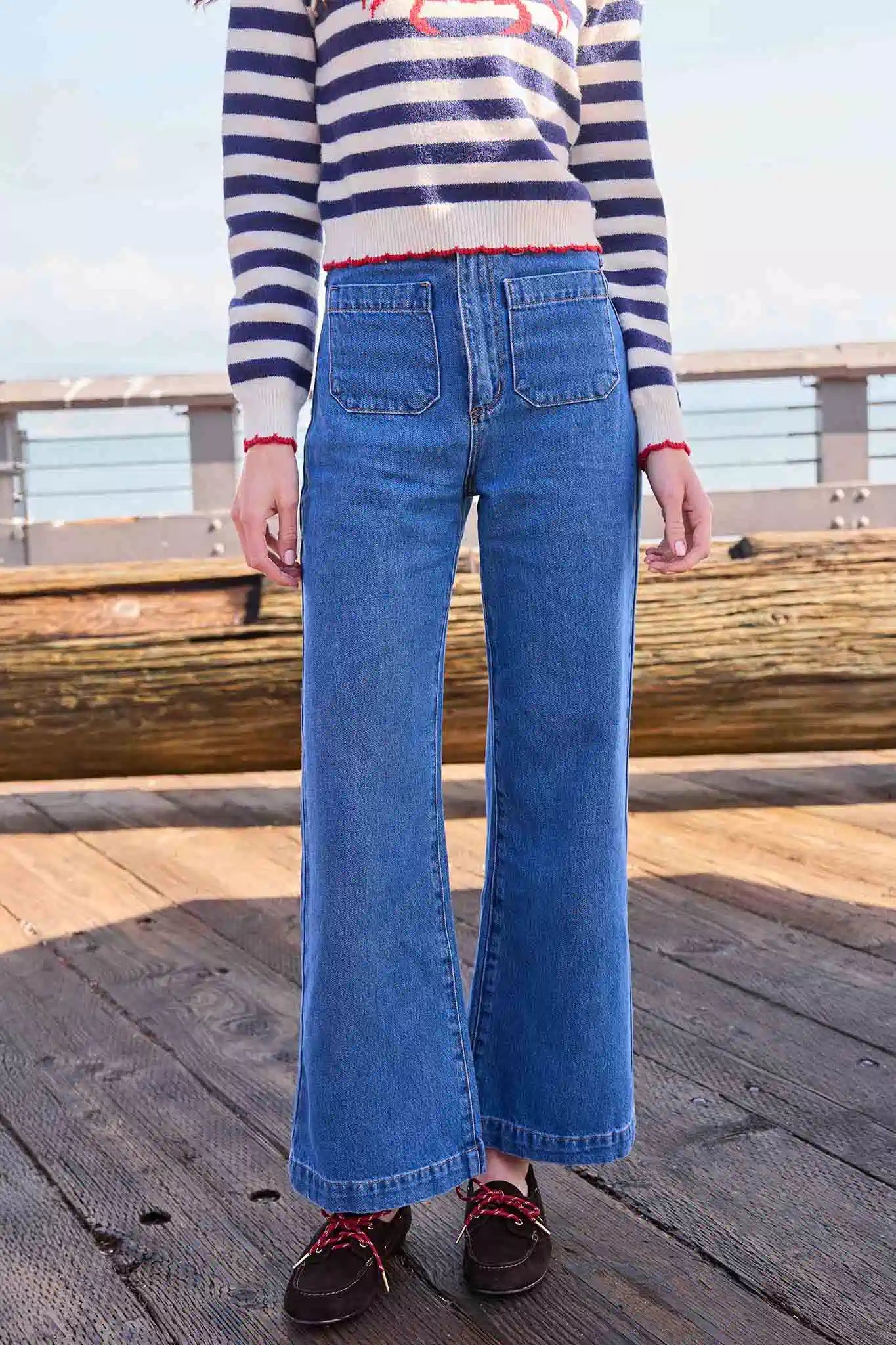 Person wearing a striped sweater and blue jeans standing on a wooden deck.