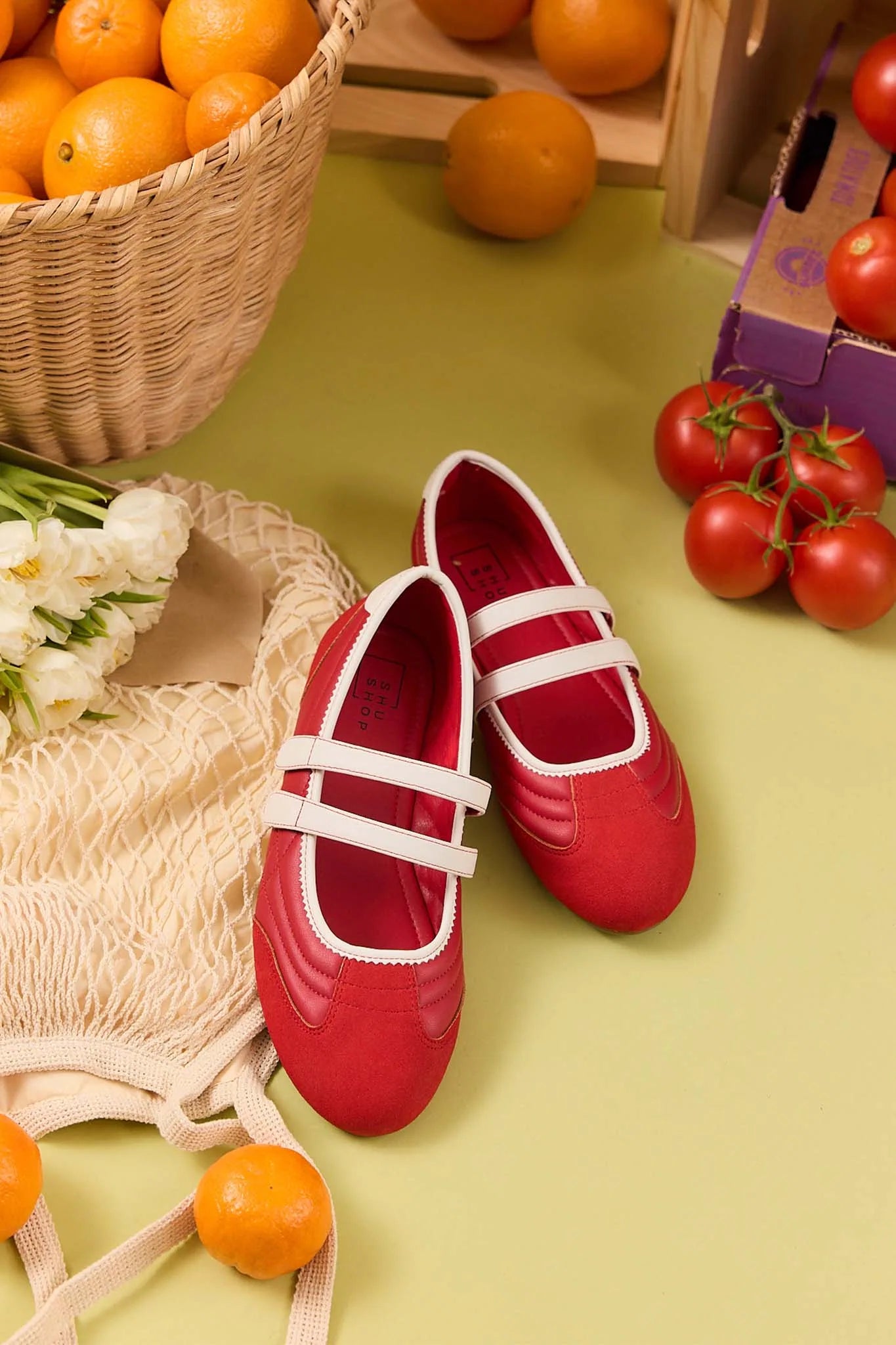 Red shoes with white straps on a green surface with fruits and flowers.